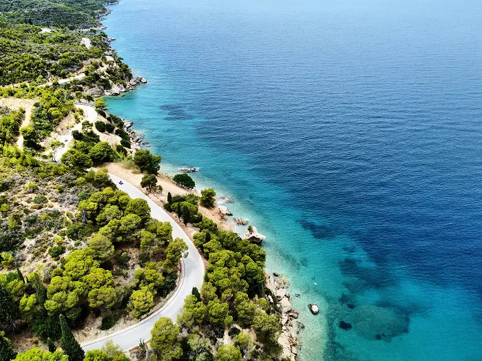 Eine Asphaltstraße verläuft entlang einer grünen, bewaldeten Küste.
