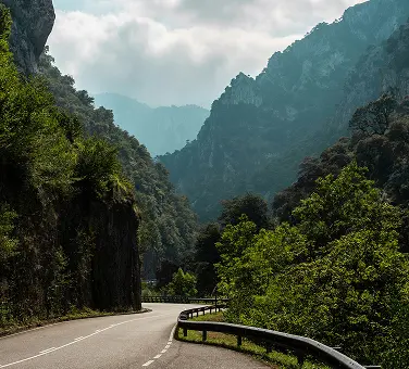 Eine Asphaltstraße verläuft durch bewaldete Berge.