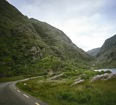 Eine kurvige Asphaltstraße führt durch grün bewachsene Berge.