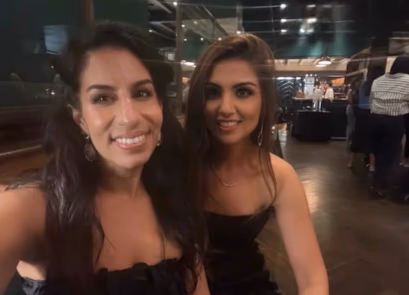 Two young women in black dresses smiling and posing for a selfie in a dimly lit restaurant or bar.