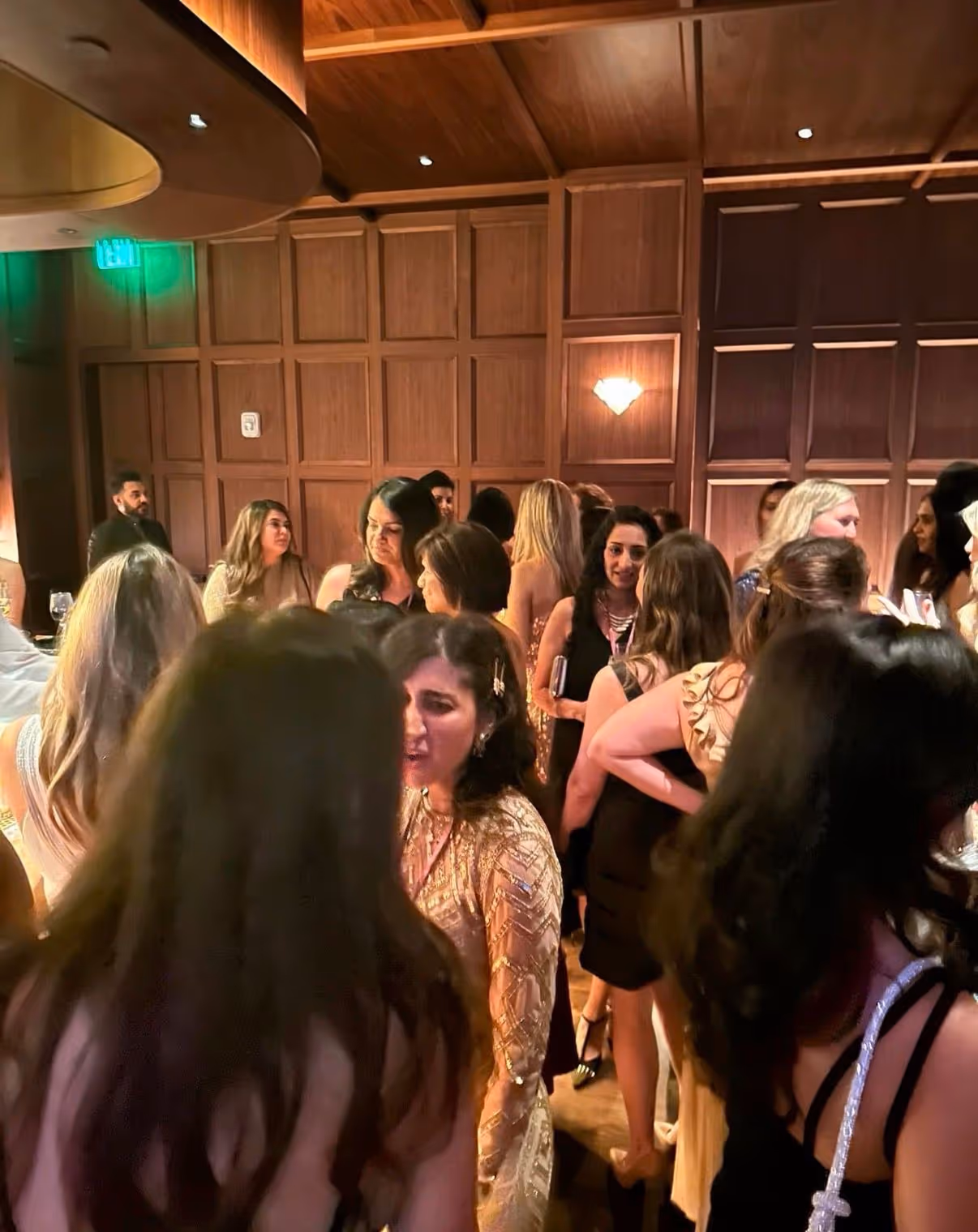 Group of people socializing indoors in a warmly lit room with wood-paneled walls.