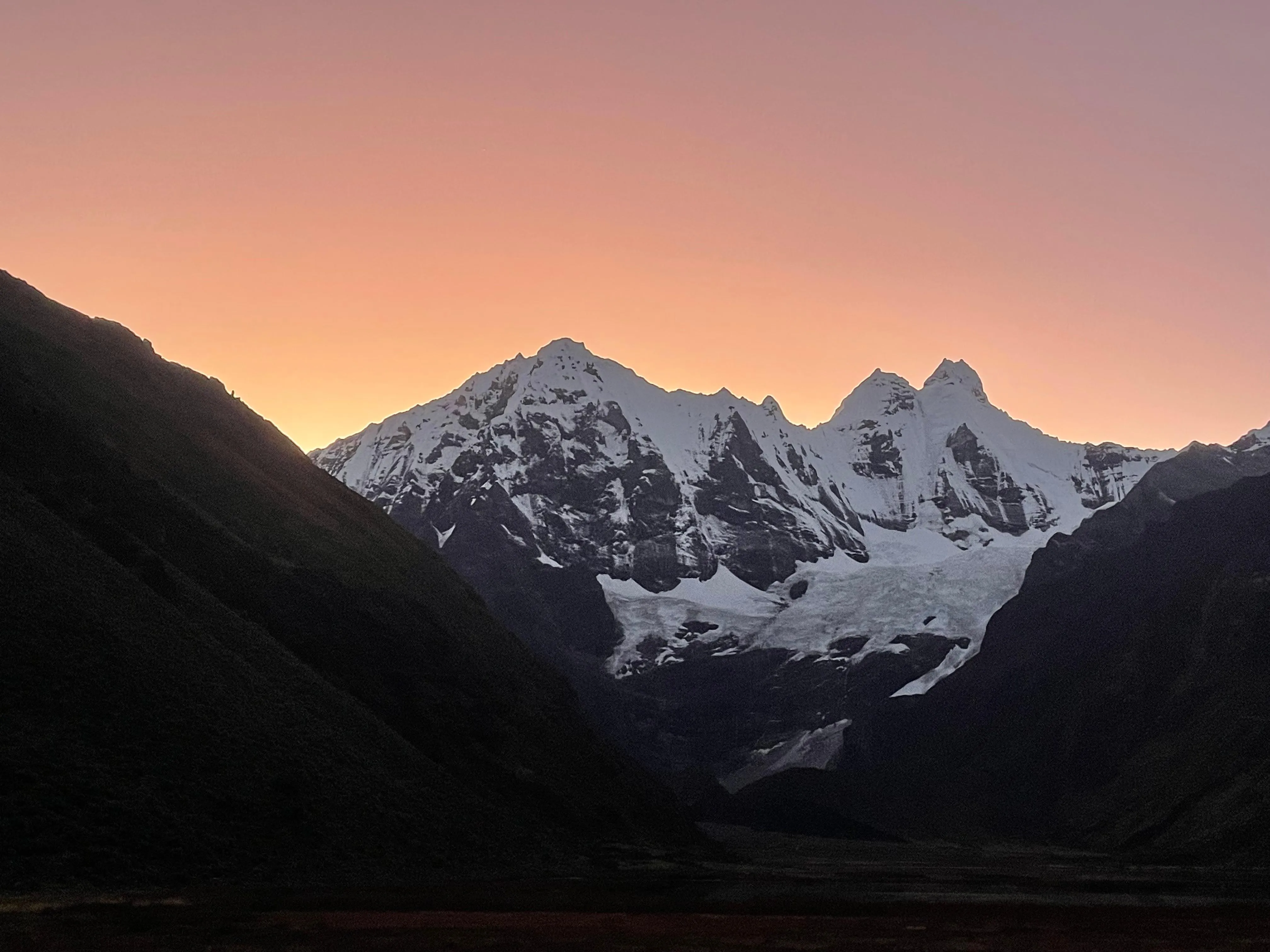 Besneeuwde bergtoppen bij zonsondergang met een oranje en paarse lucht.