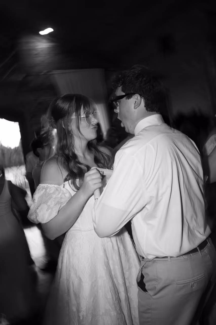 Black and white photo of a woman and man dancing closely at a social event, both wearing glasses.