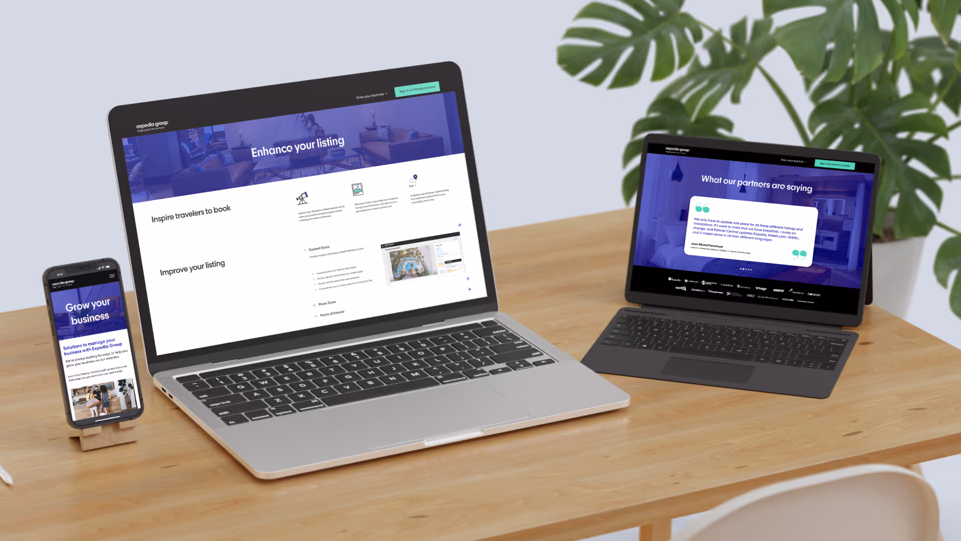 Expedia Group business platform displayed on laptop, tablet, and smartphone on wooden desk with monstera plant in background.