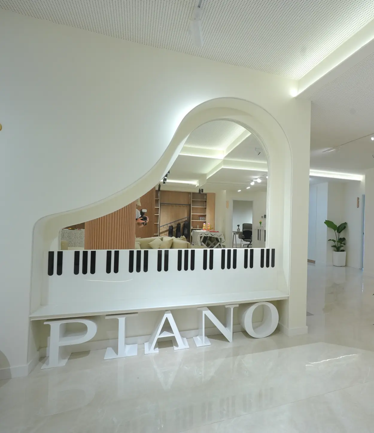 Espejo grande en forma de piano con teclas negras y blancas y letras blancas formando la palabra PIANO en el suelo de un espacio interior moderno y luminoso.