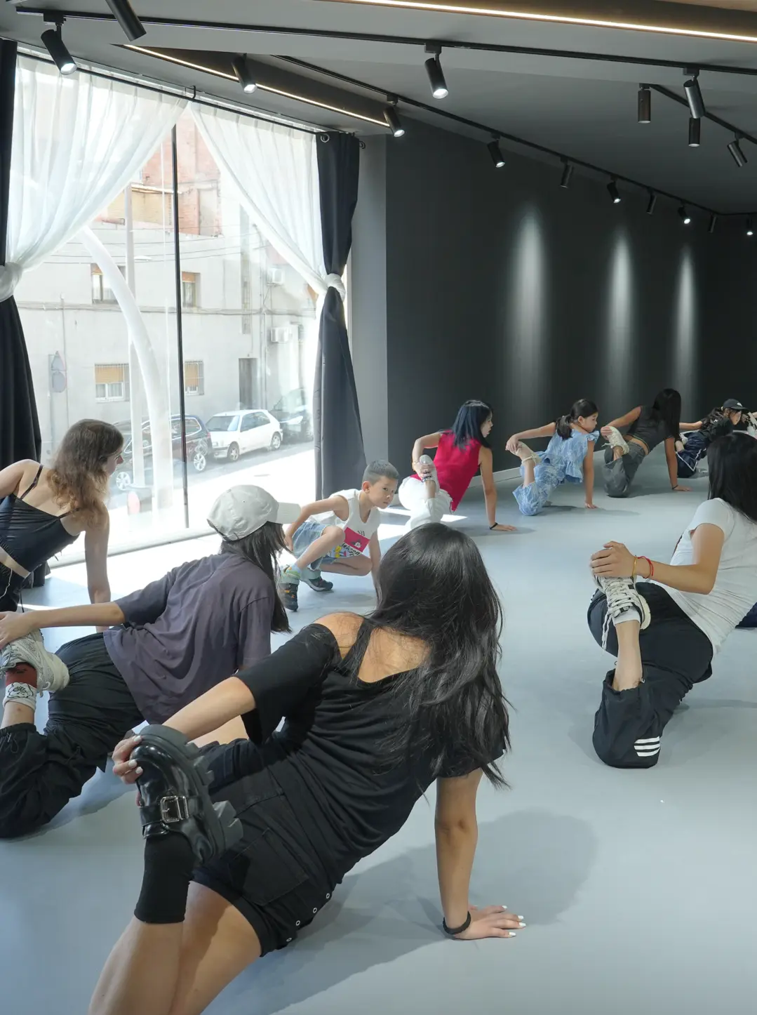 Grupo de personas en una clase de estiramientos en un estudio con paredes oscuras y ventana grande.