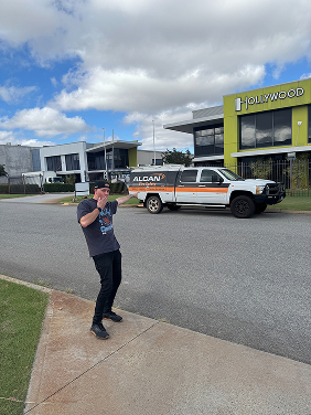 Man talking on phone standing on a sidewalk near street with parked truck and modern office buildings.