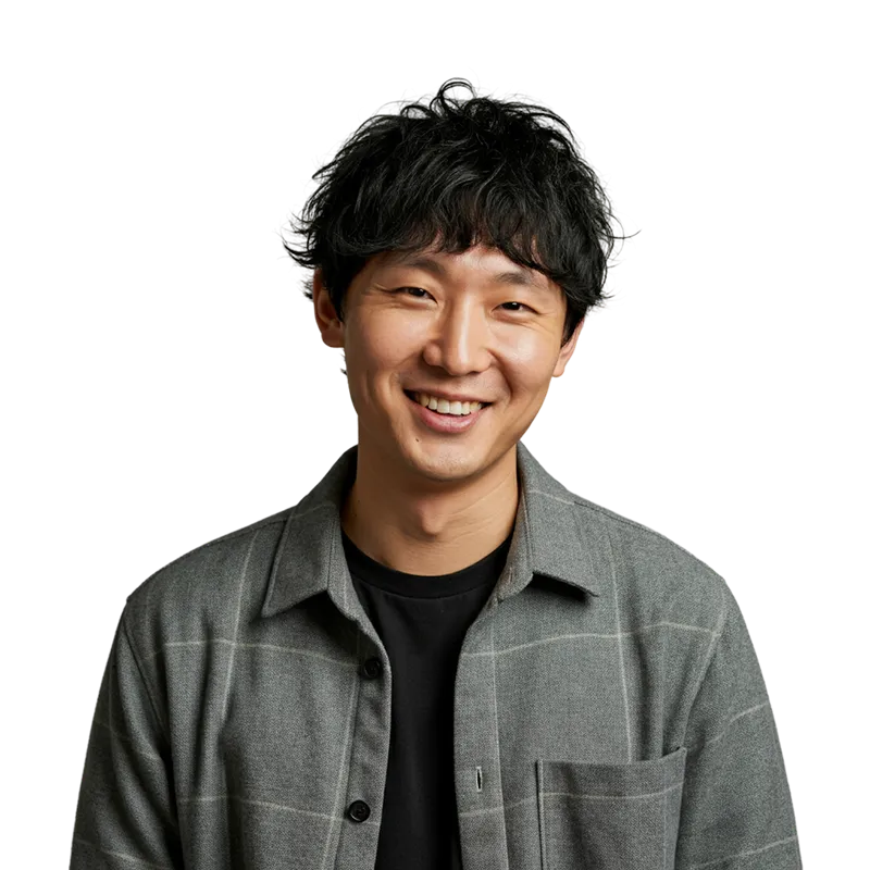 Smiling young man with black curly hair wearing a gray plaid jacket over a black shirt.