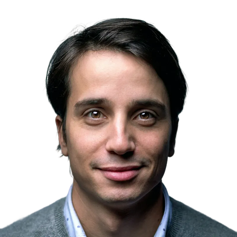 Young man with dark hair and brown eyes smiling gently, wearing a gray sweater over a collared shirt.