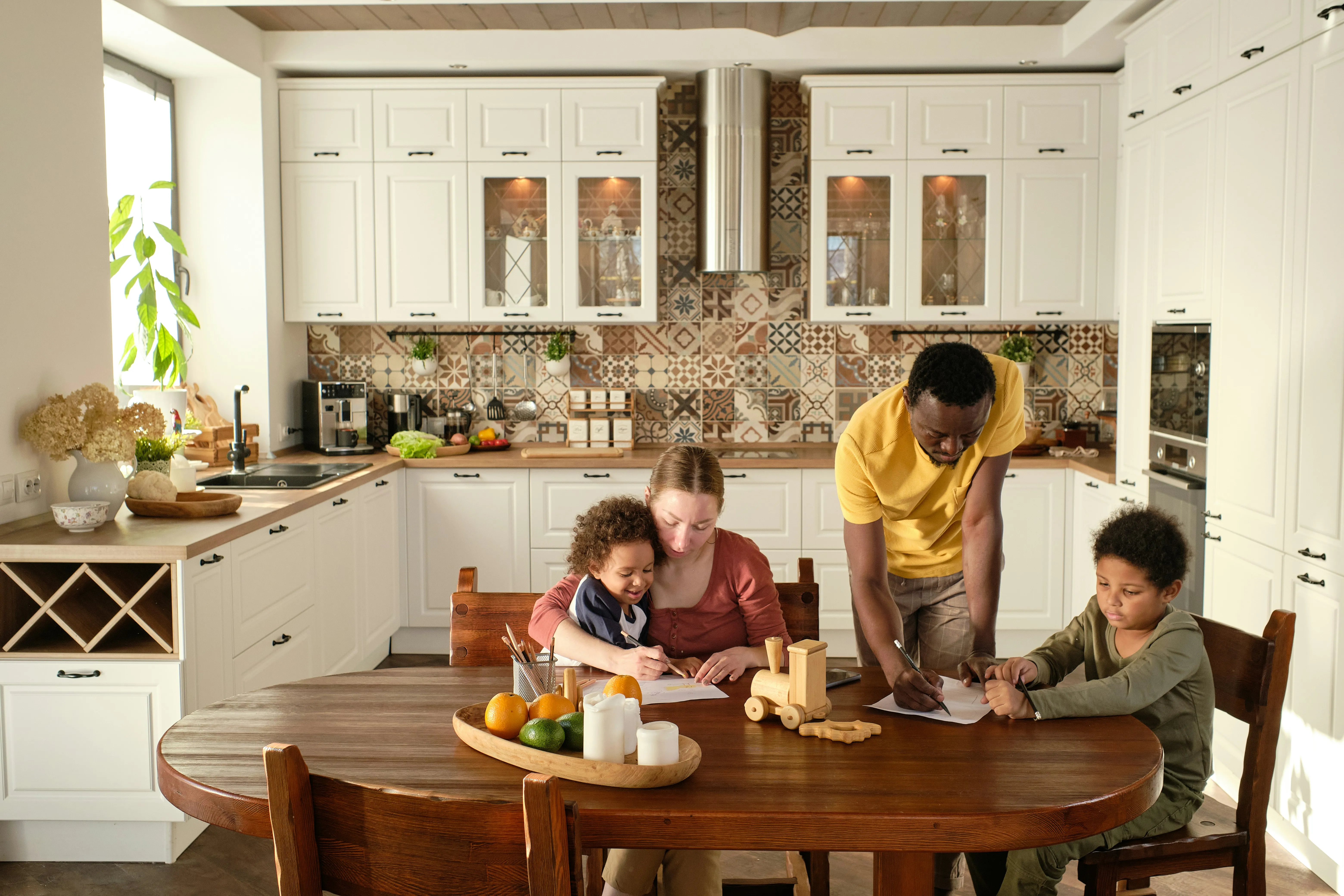 A family of four in a modern kitchen, with two children and two adults drawing together at a wooden table.