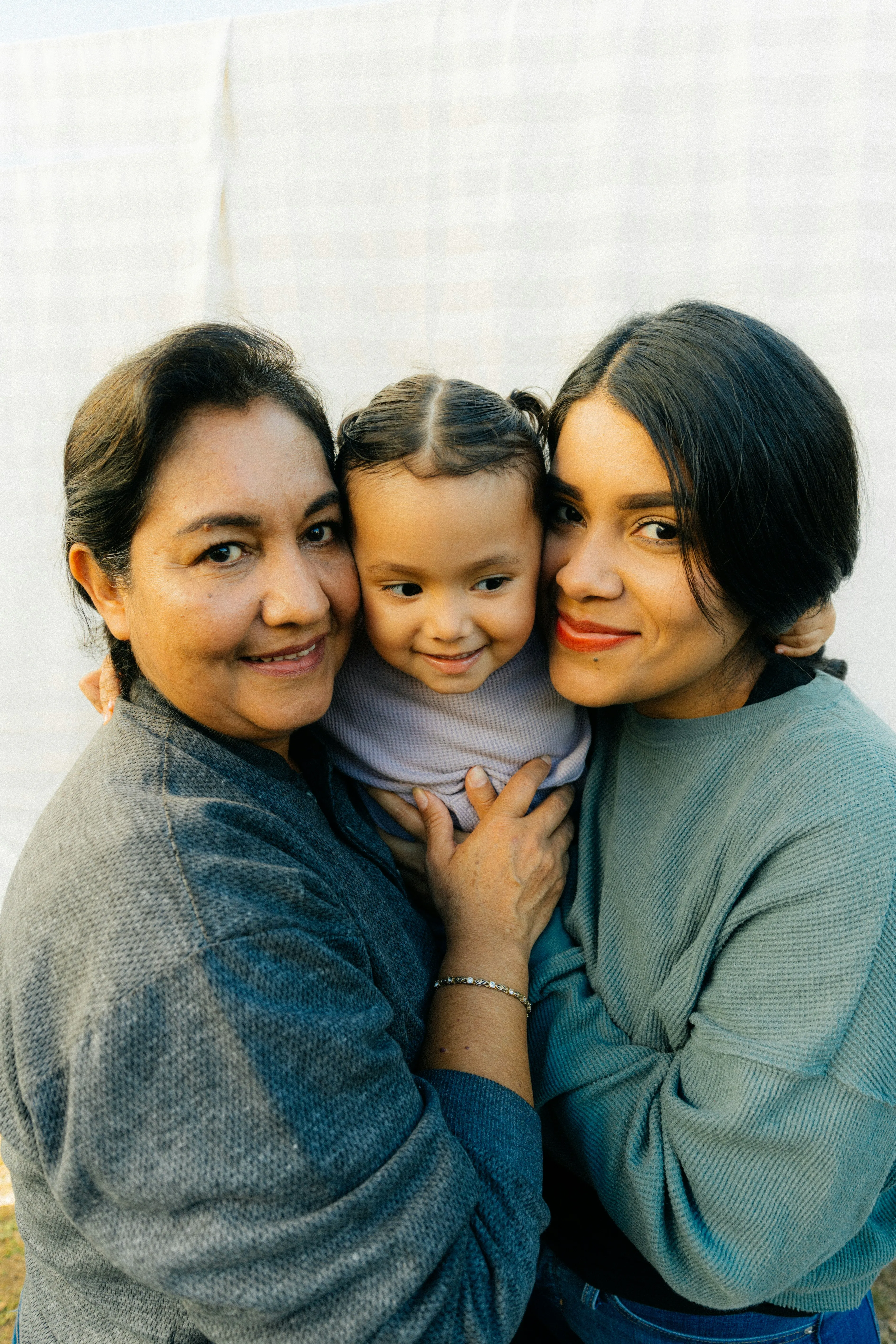 Three generations of a family smiling and hugging, including two women and a young child.