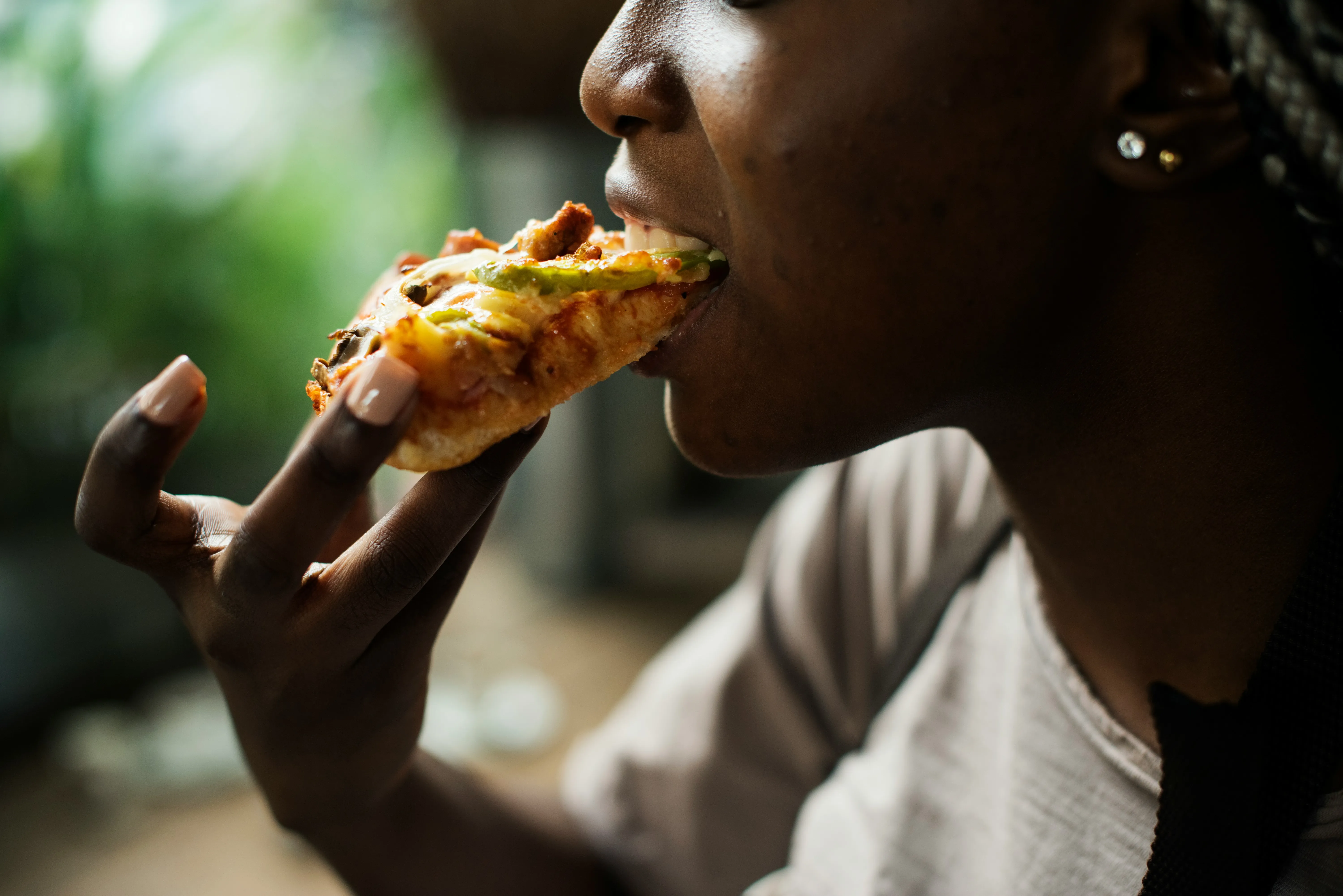 Close-up of a person biting into a slice of pizza with vegetables and cheese.