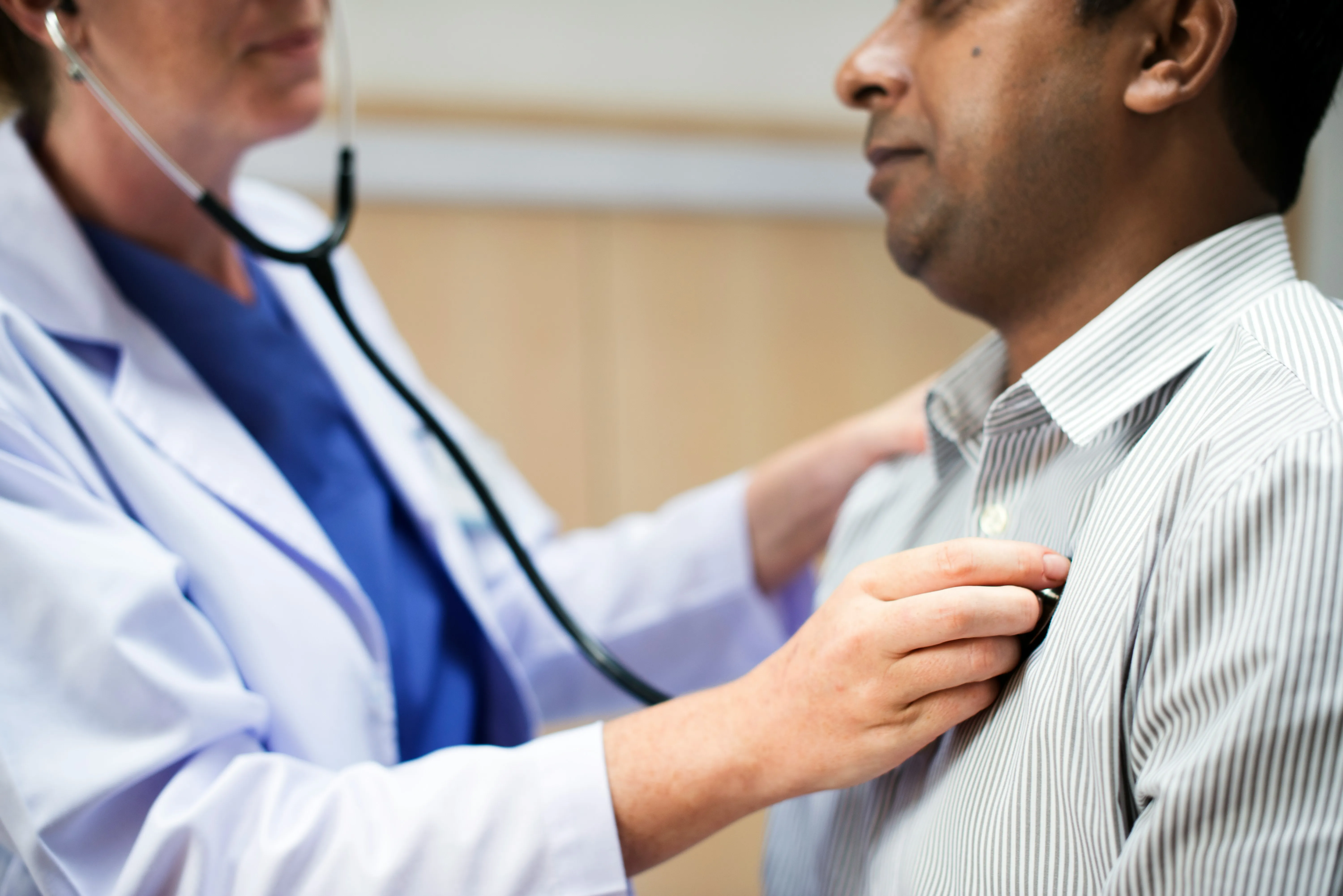 Doctor using a stethoscope to check a male patient's heartbeat during a medical exam.