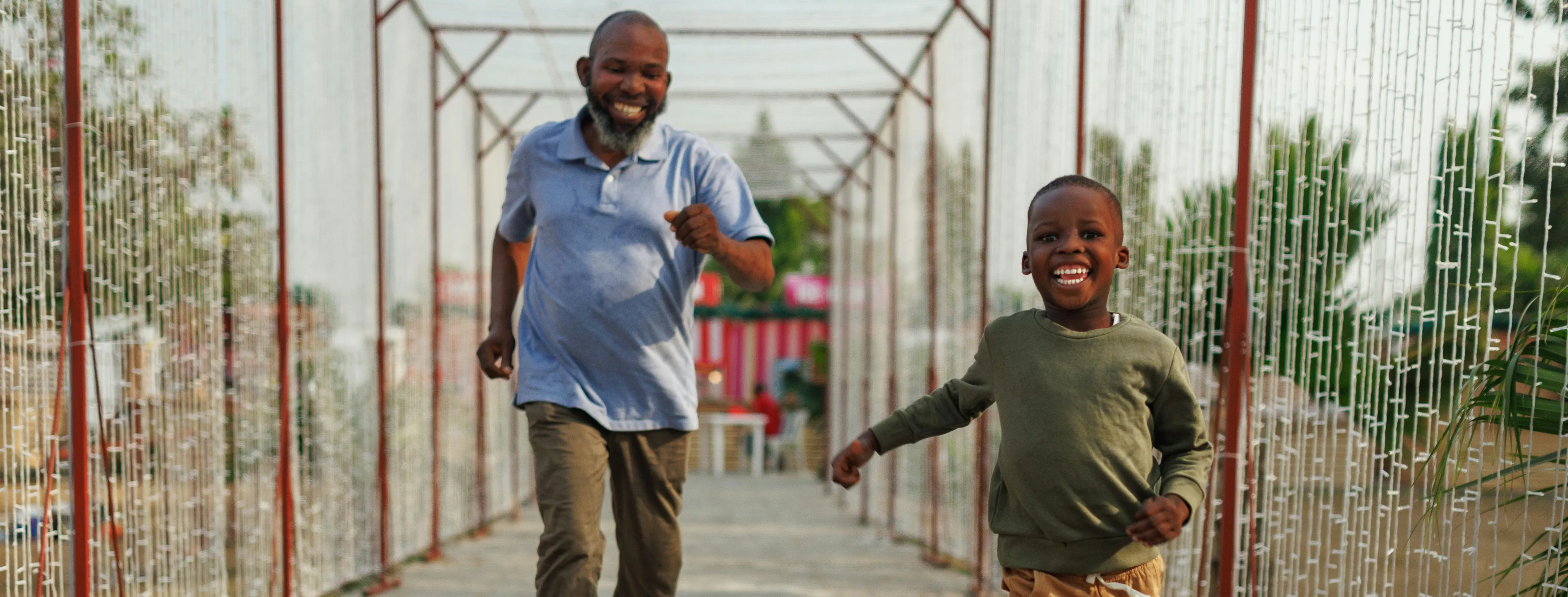 Smiling man and child running happily on a decorated outdoor walkway.