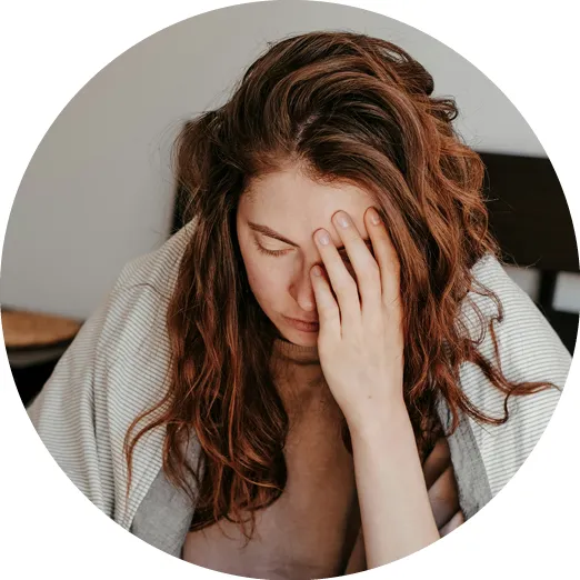 Woman with long hair wrapped in a blanket holding her face, appearing tired or stressed.