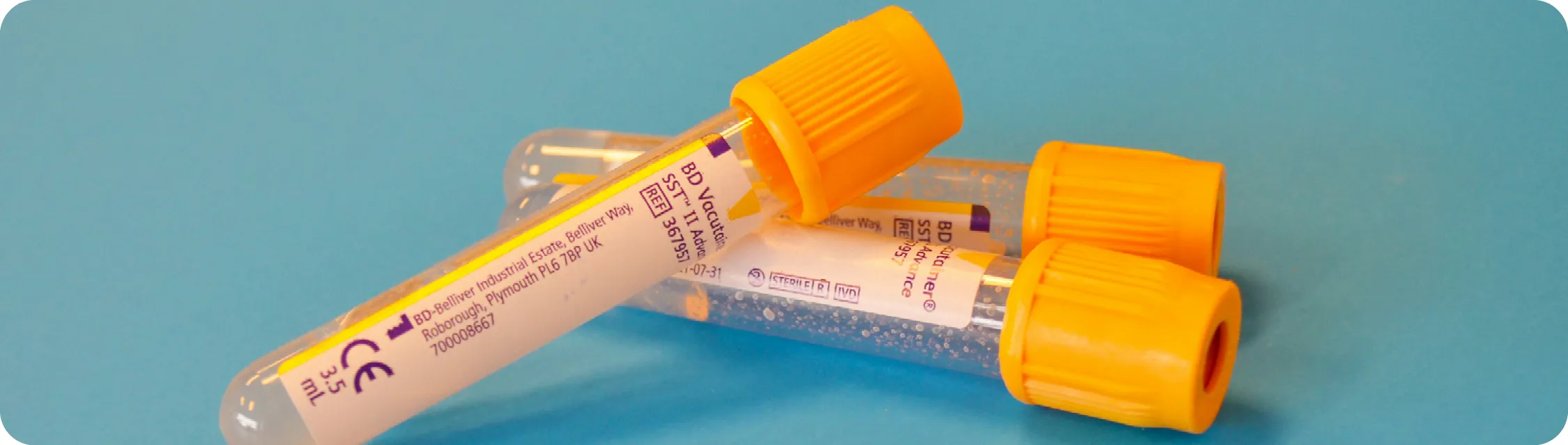 Three 3.5 mL BD Vacutainer tubes with yellow caps on a blue surface.