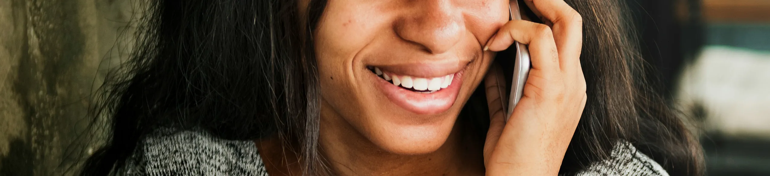 Smiling woman with long hair holding phone to ear during a call.