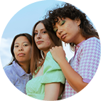 Three young women standing closely together, posing with a blue sky background.