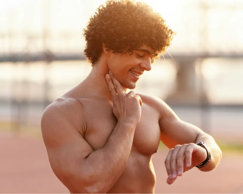 Shirtless man checking pulse on neck while looking at a smartwatch during outdoor workout.