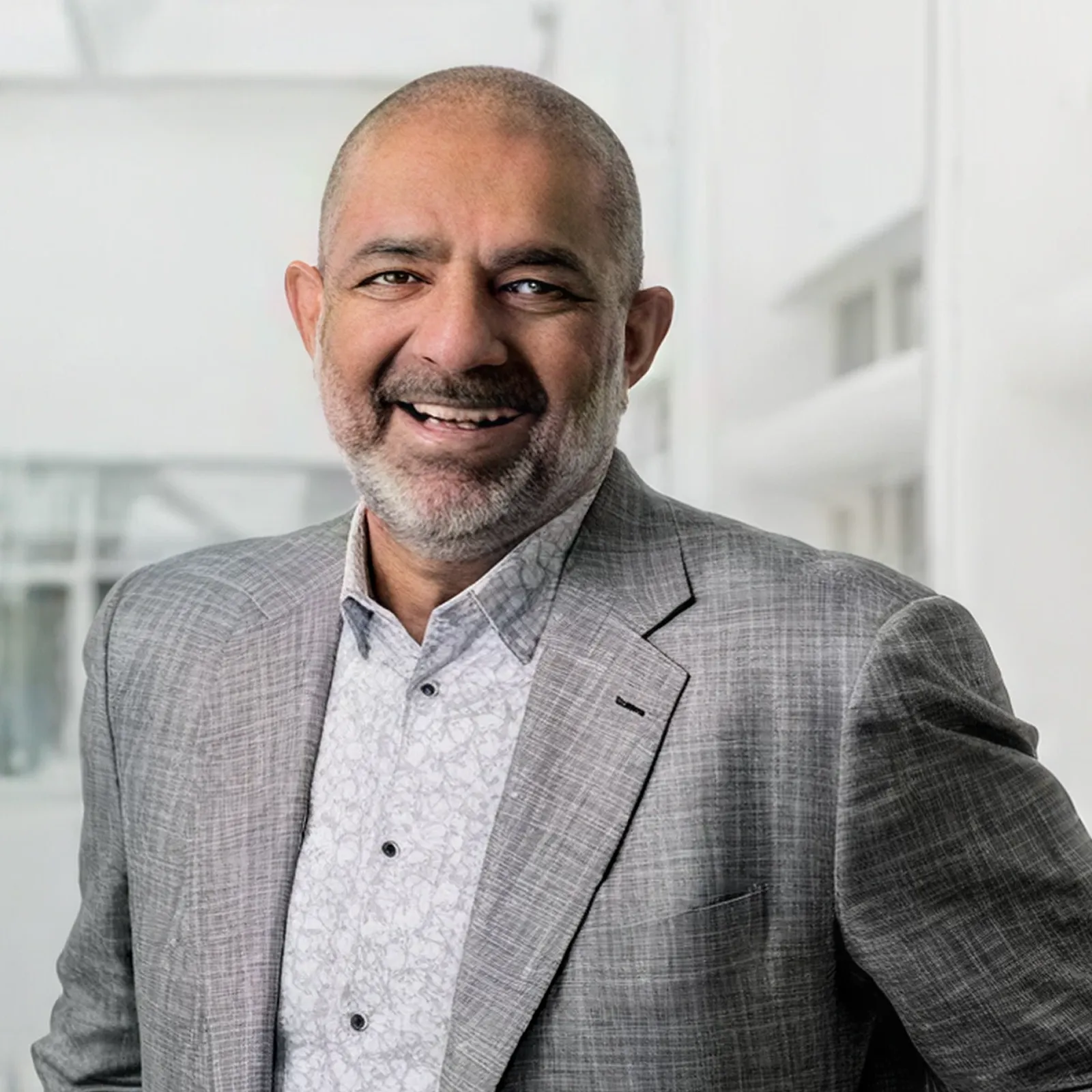 Smiling middle-aged man with short hair and beard wearing a grey suit jacket and patterned shirt.