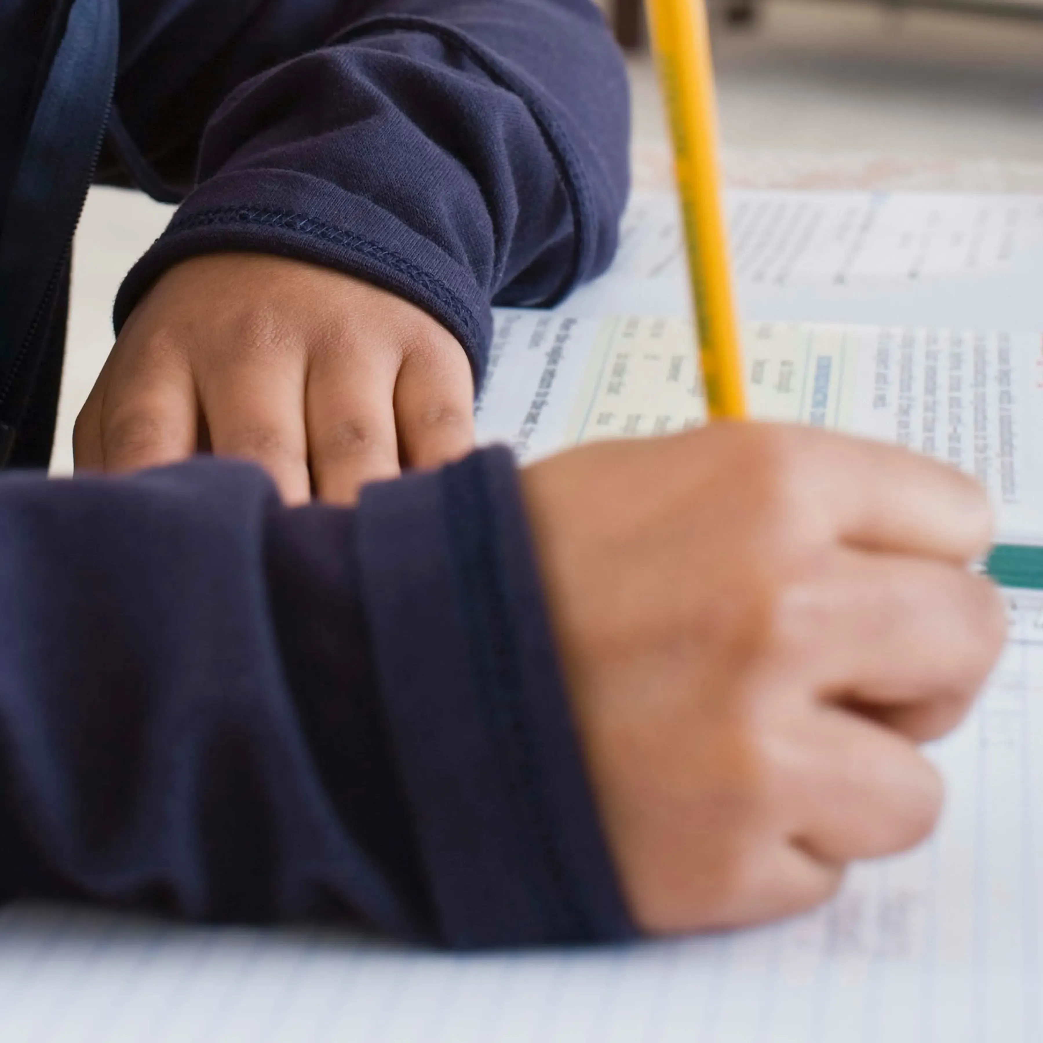 Close-up of a child’s hands writing with a yellow pencil on a workbook.