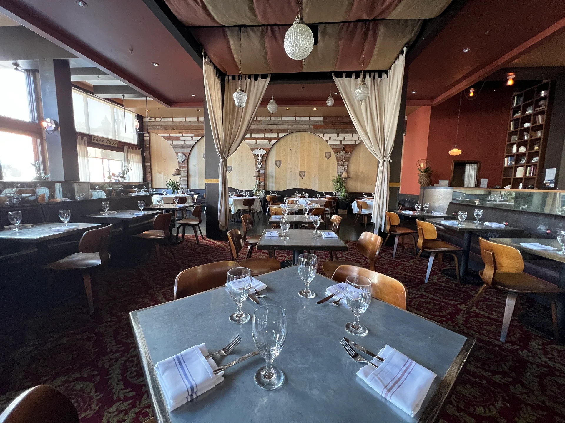 A cozy restaurant interior featuring several tables and chairs arranged for dining, with a stylish ceiling fixture overhead. The space is designed with modern furniture and has a welcoming atmosphere.