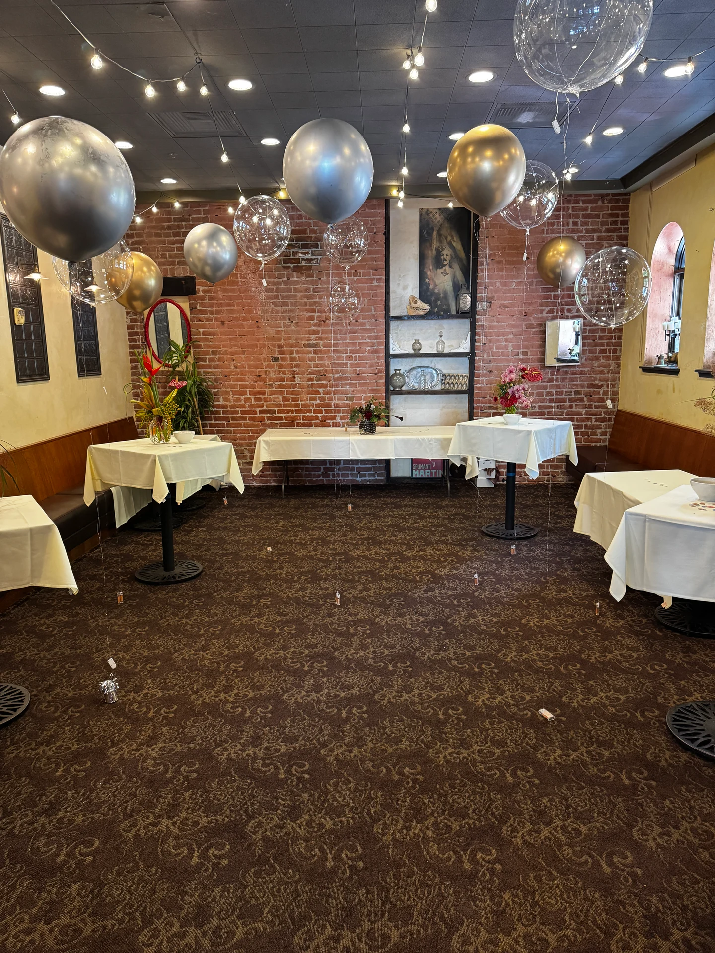 A room featuring several tables adorned with balloons, showcasing an indoor setting with chairs and a designed ceiling.