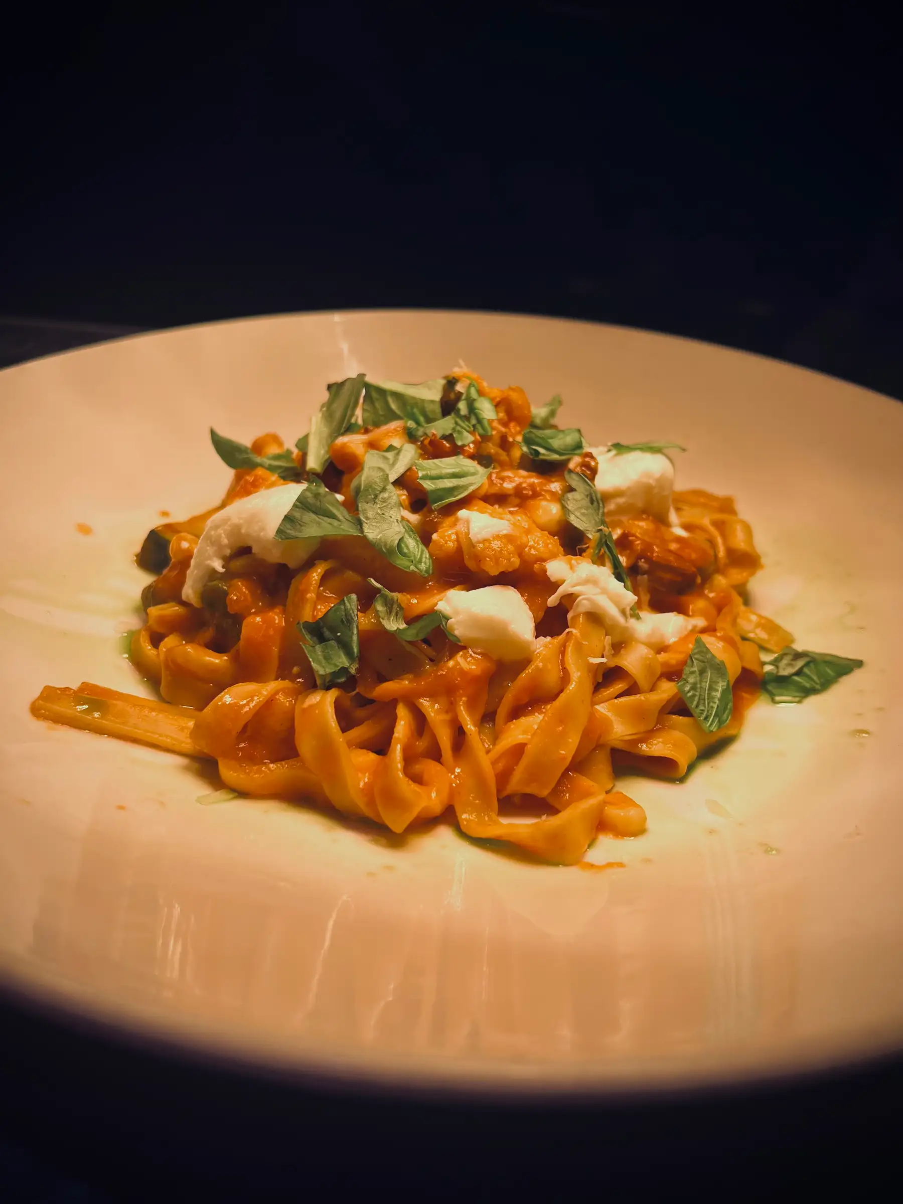 A plate of tagliatelle pasta with a rich tomato sauce, topped with fresh basil leaves and dollops of creamy cheese, creating a warm, inviting presentation.