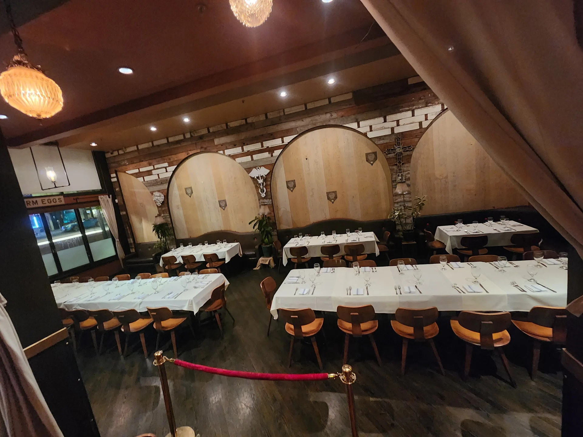 Elegant restaurant with round wooden decor and white tablecloths set for dining. Soft lighting and dark wood floors create a cozy, refined atmosphere.