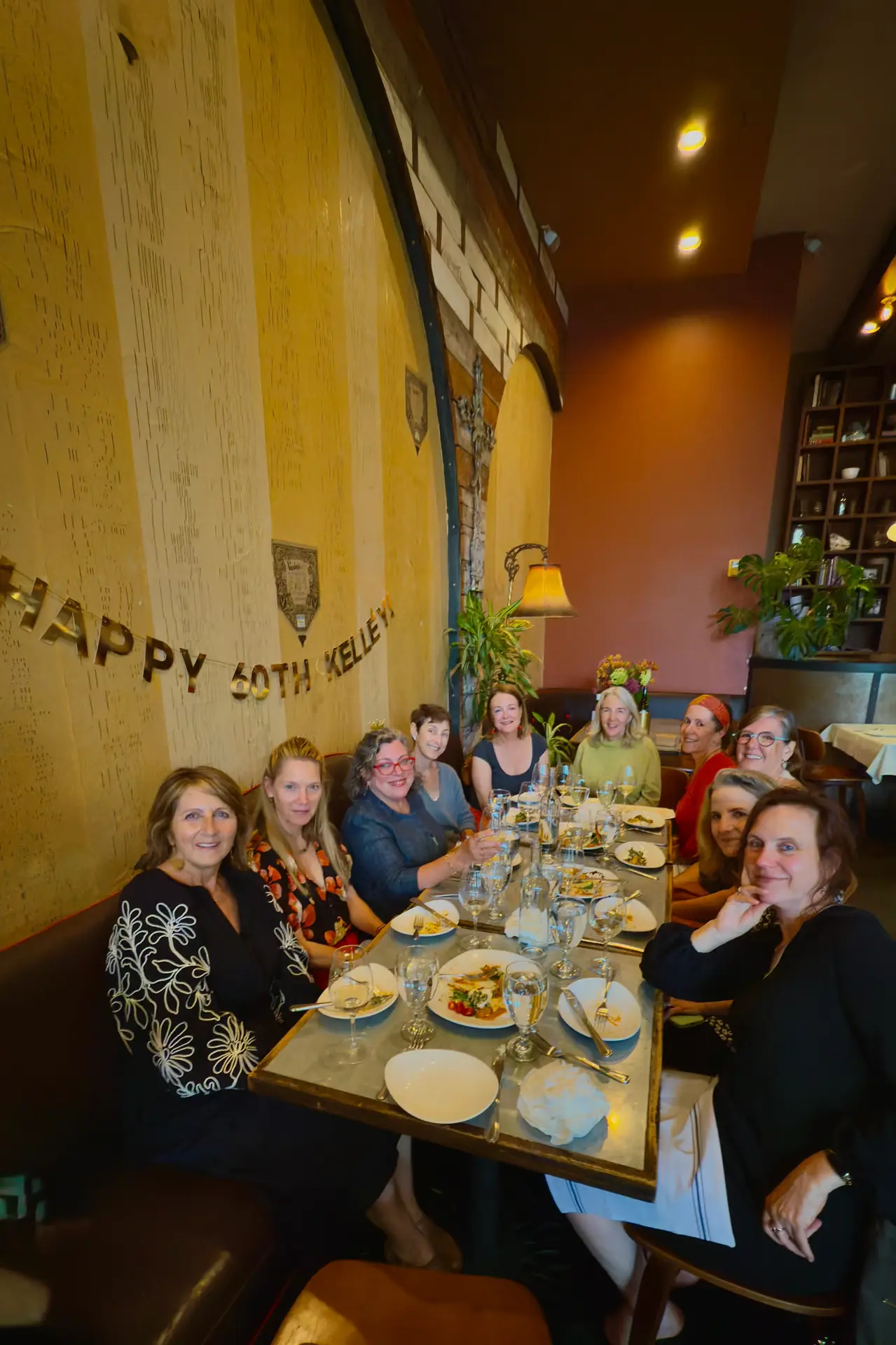 A group of women sit around a table with plates of food and wine glasses.