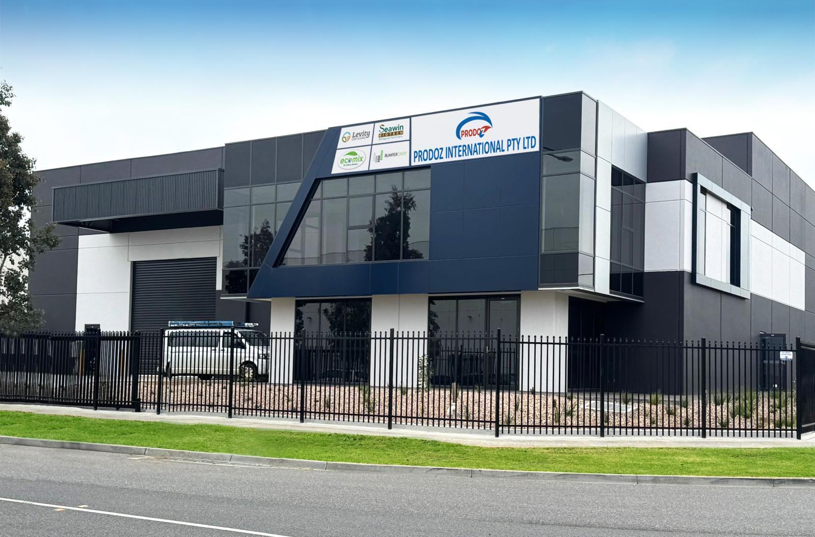 Modern commercial building with a black fence, signage for Prodoz International Pty Ltd and other companies, and a white van parked inside.