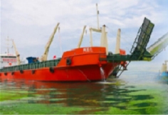 Red cargo ship docked near cranes under a cloudy sky.