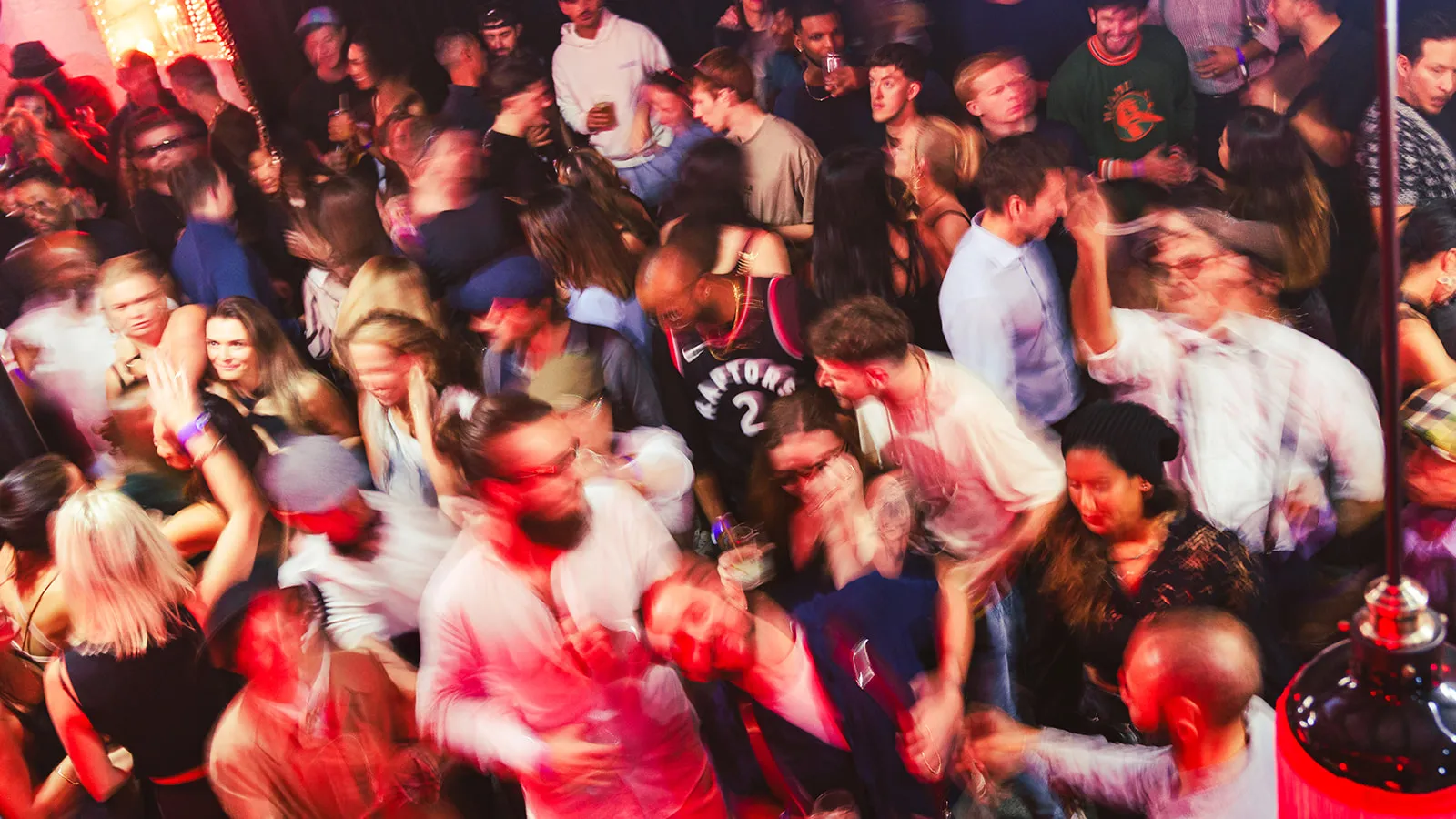 Crowded nightclub dance floor with people dancing and socializing under colorful lighting.