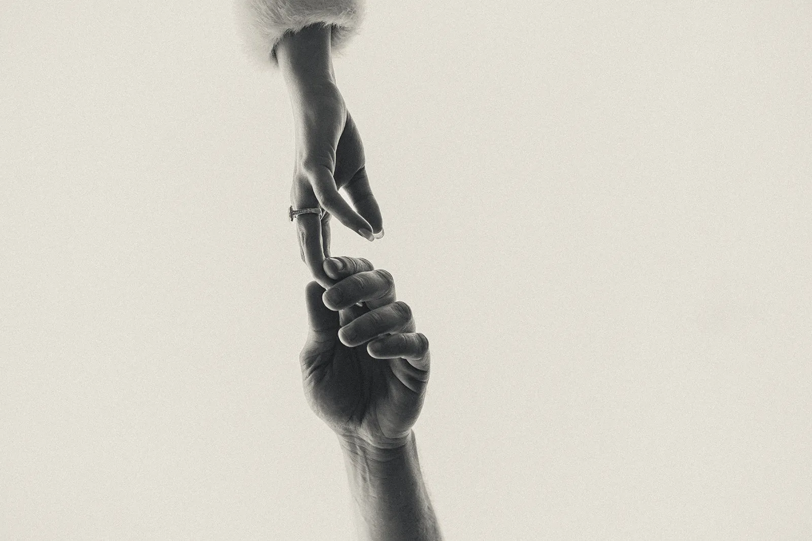 Two hands reaching towards each other with fingers gently touching on a plain light background.