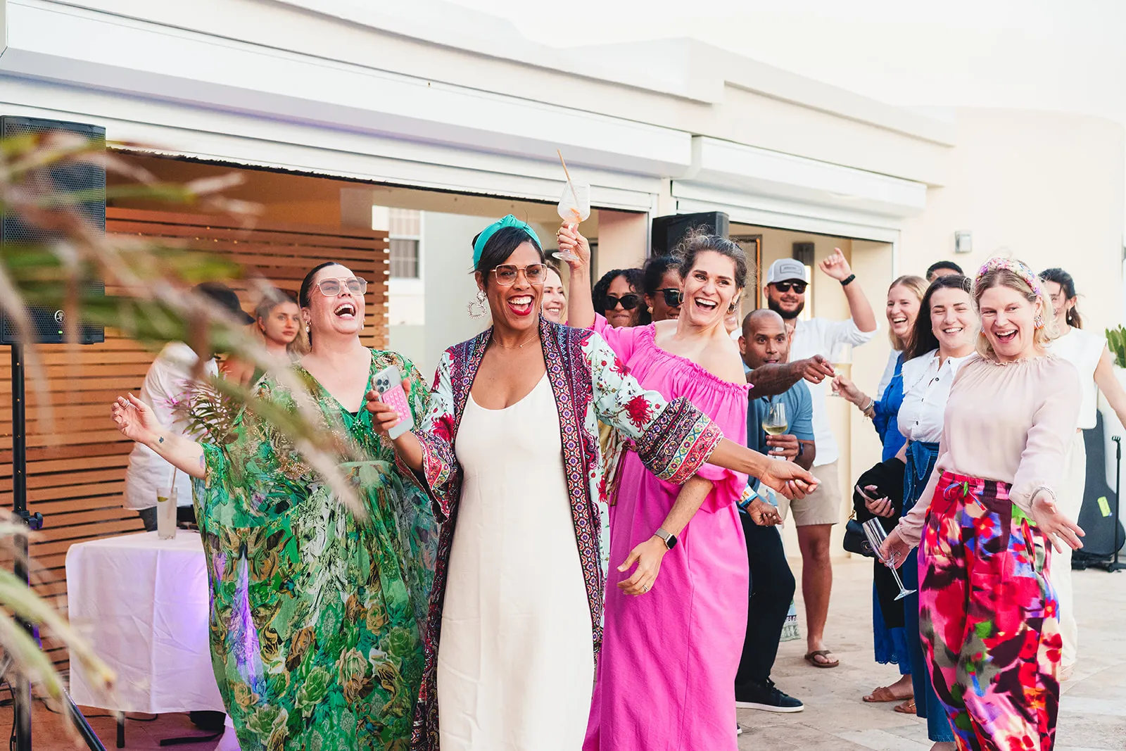 Group of diverse people dressed in colorful outfits smiling and dancing at an outdoor party.