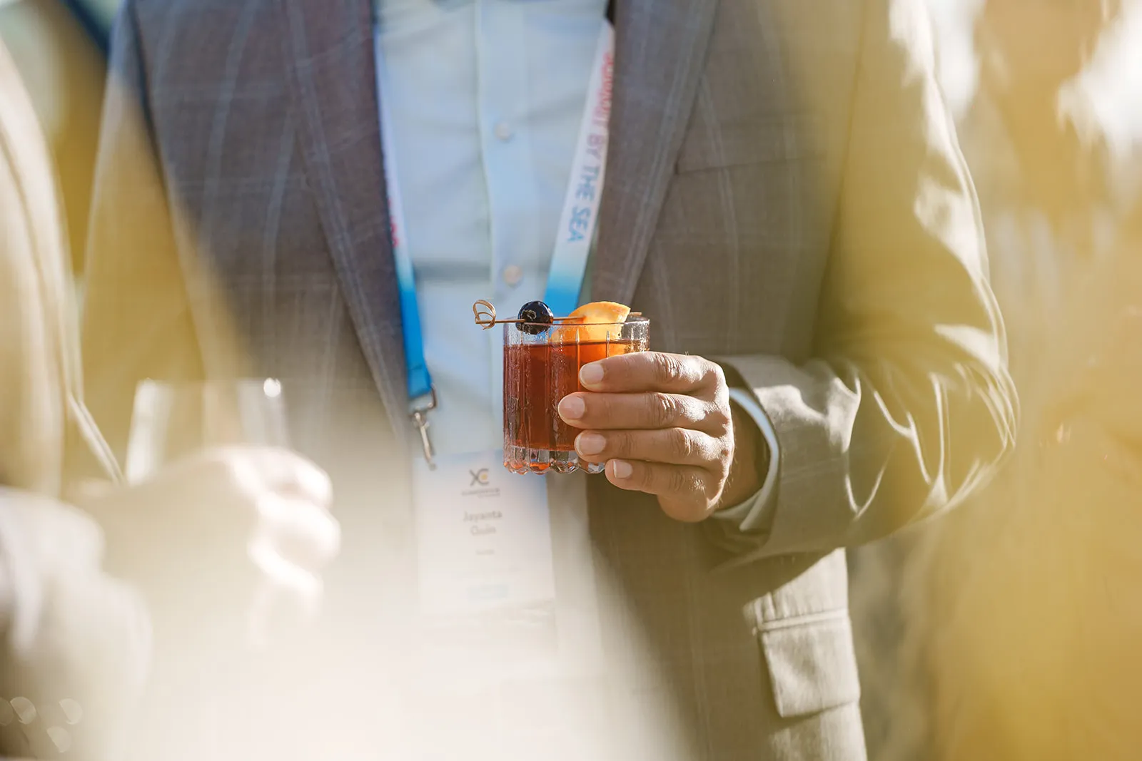 Person in a blazer holding a cocktail glass garnished with a cherry and orange slice.