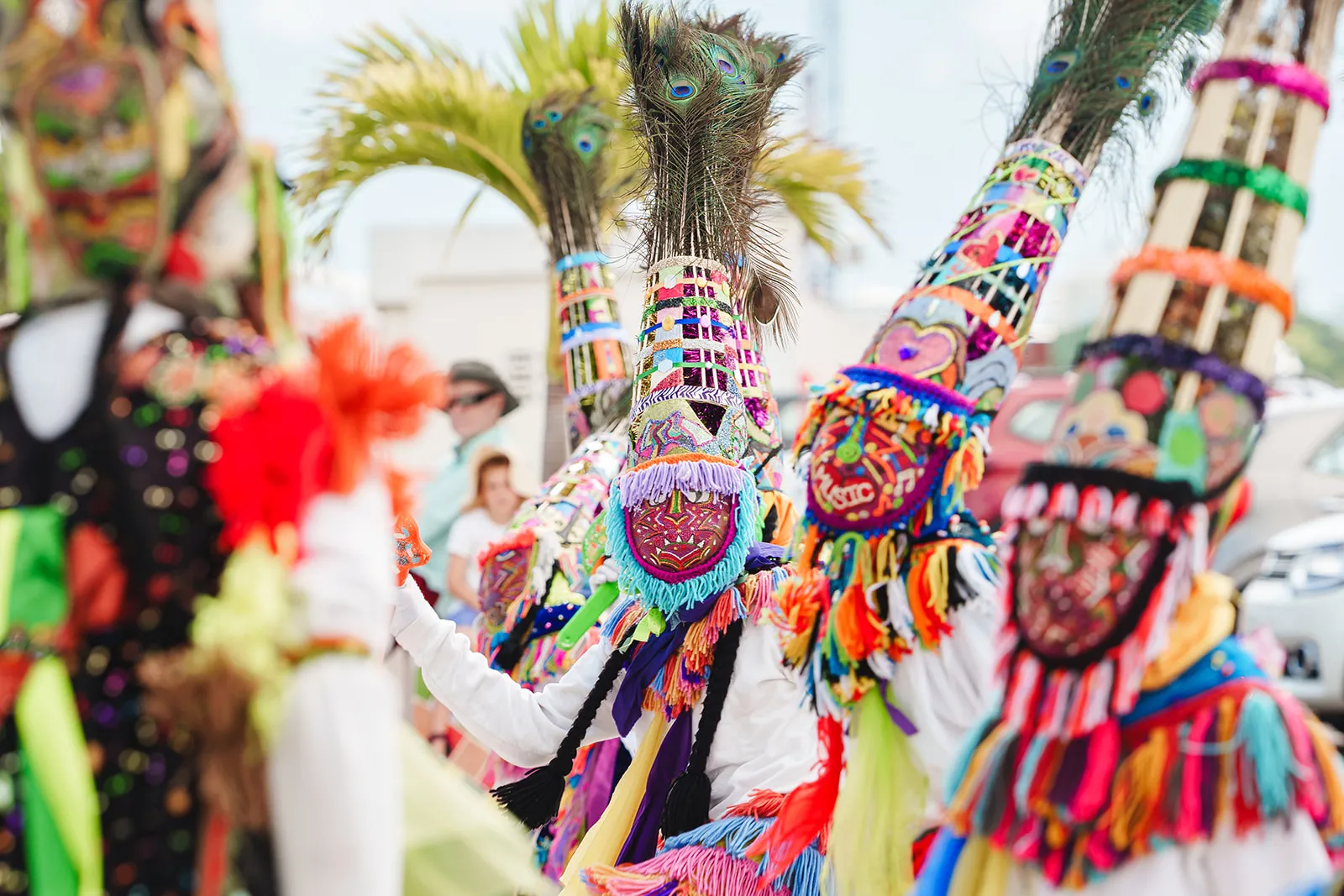 Group of people wearing colorful traditional costumes with tall headdresses decorated with feathers and vibrant patterns during a festive outdoor event.