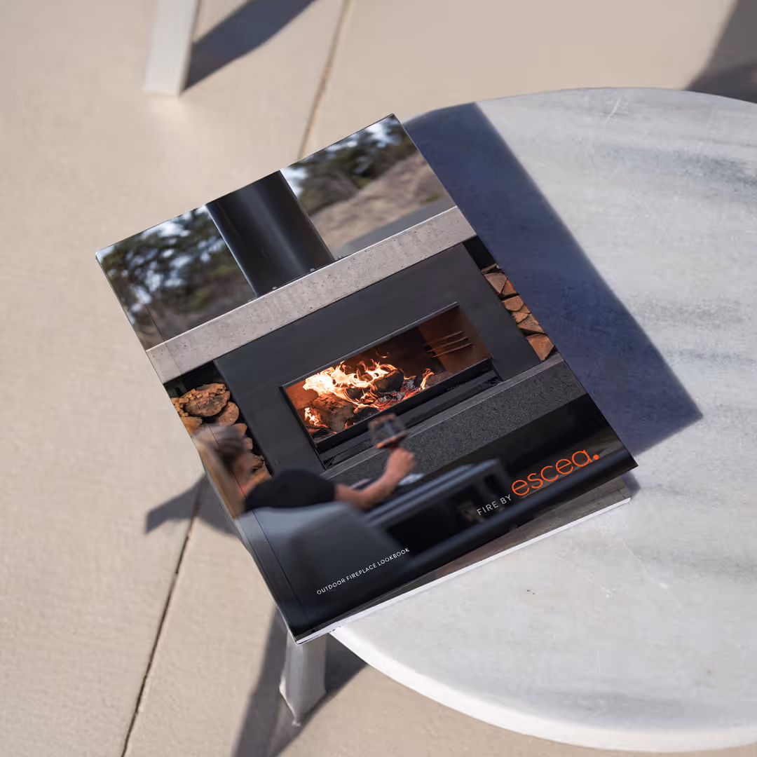 Book on a round table showing outdoor fireplace with fire and person holding a glass of wine.