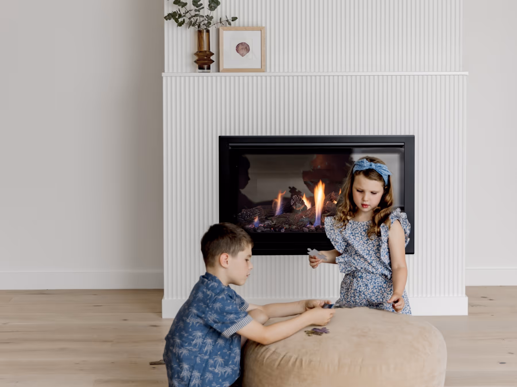 Modern gas fireplace with realistic burning logs set in a light-coloured wall next to a wooden side table with books.