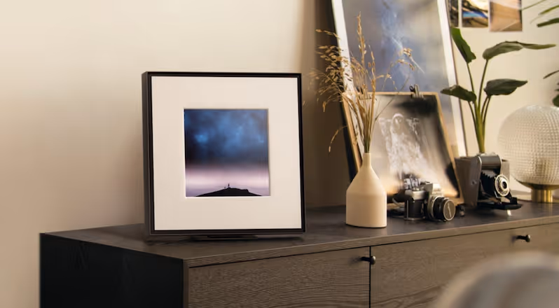 Modern gas fireplace with realistic burning logs set in a light-coloured wall next to a wooden side table with books.