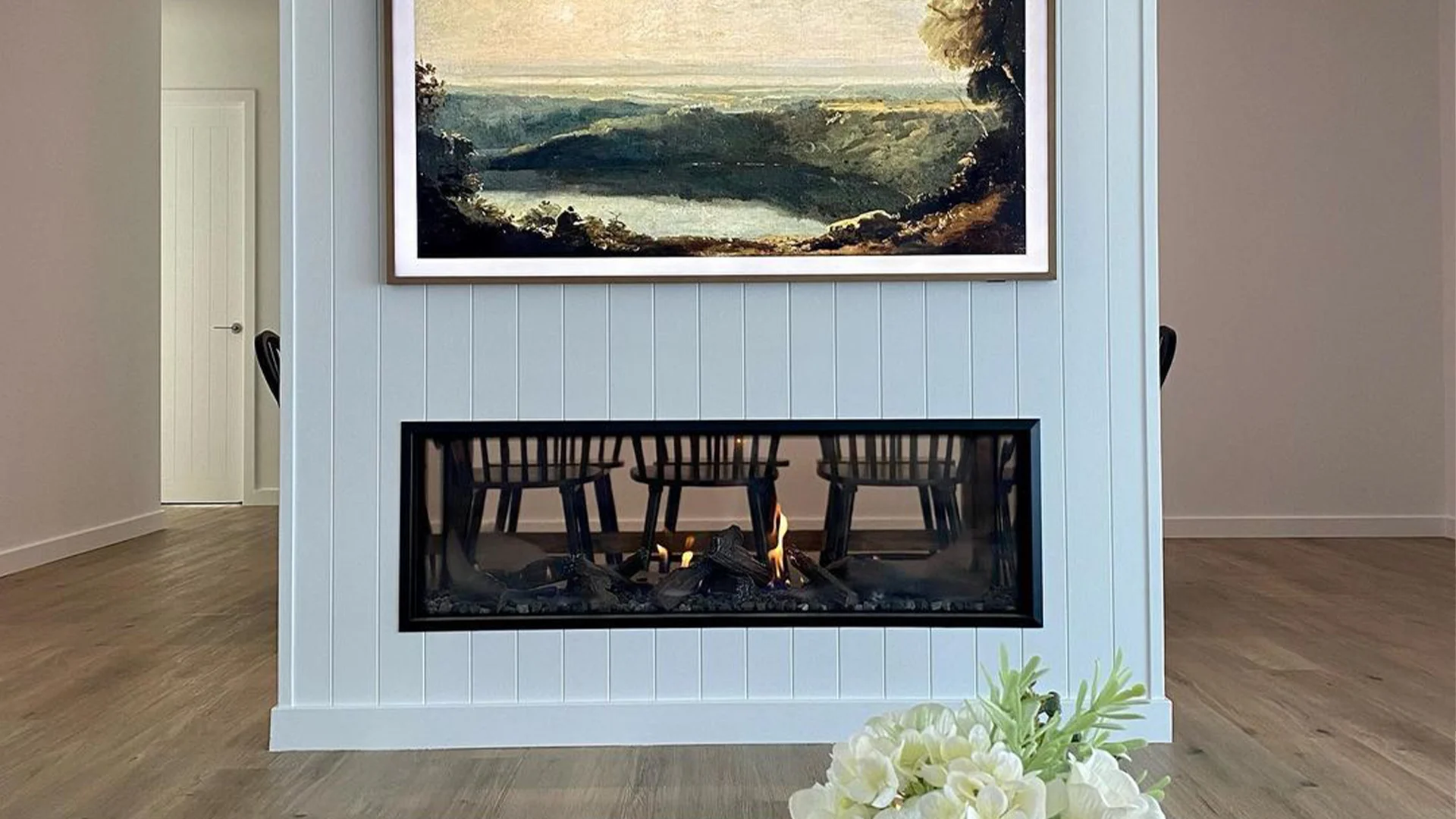 Modern gas fireplace with realistic burning logs set in a light-coloured wall next to a wooden side table with books.