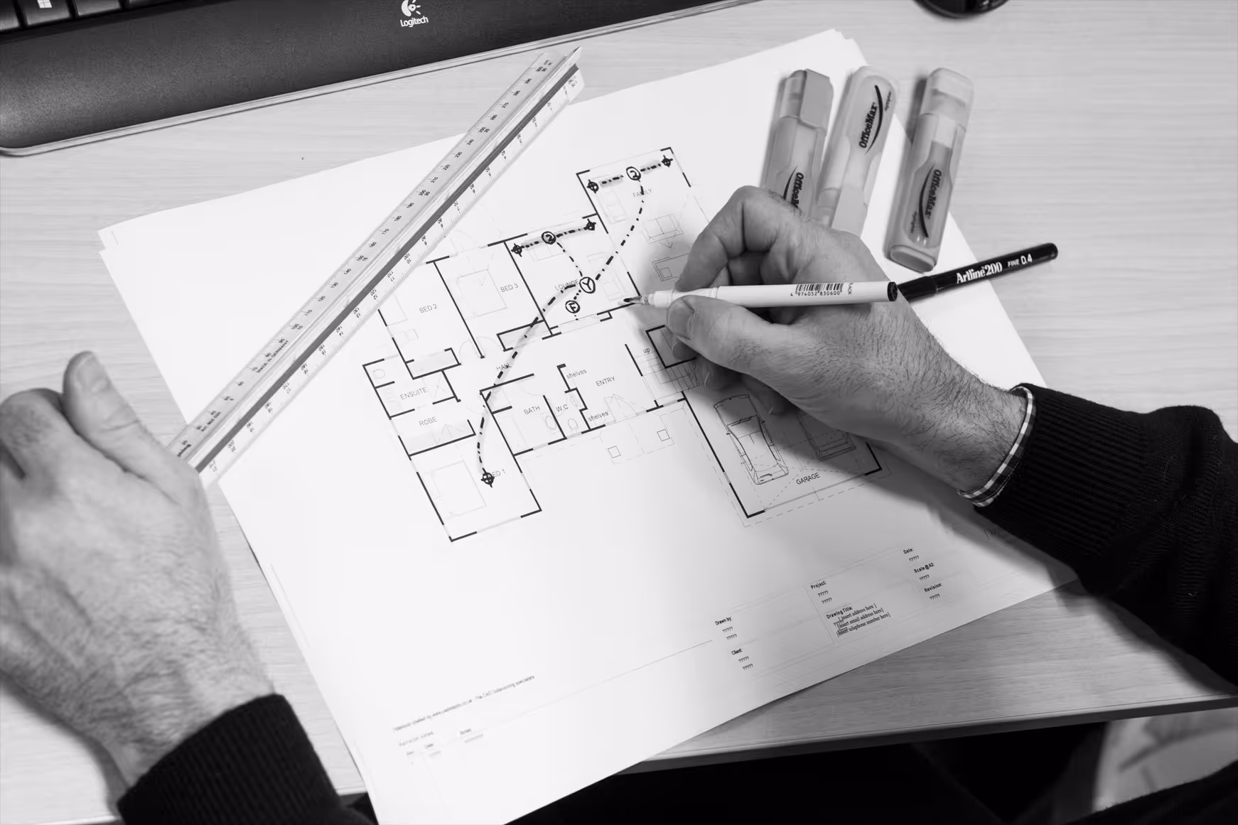 Hands drawing on a house floor plan with a pen and ruler on a desk with highlighters.