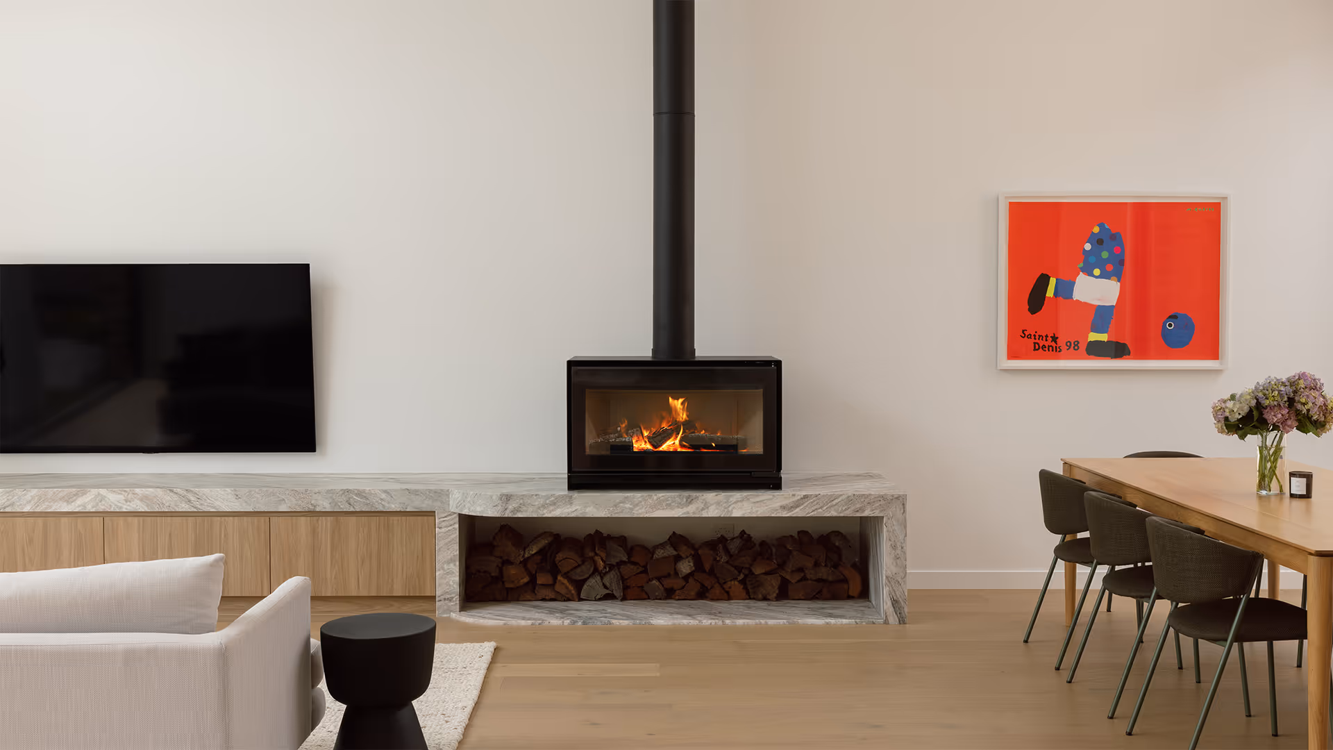 Cheminée à gaz moderne avec des bûches réalistes, encastrée dans un mur de couleur claire, à côté d'une table d'appoint en bois avec des livres.