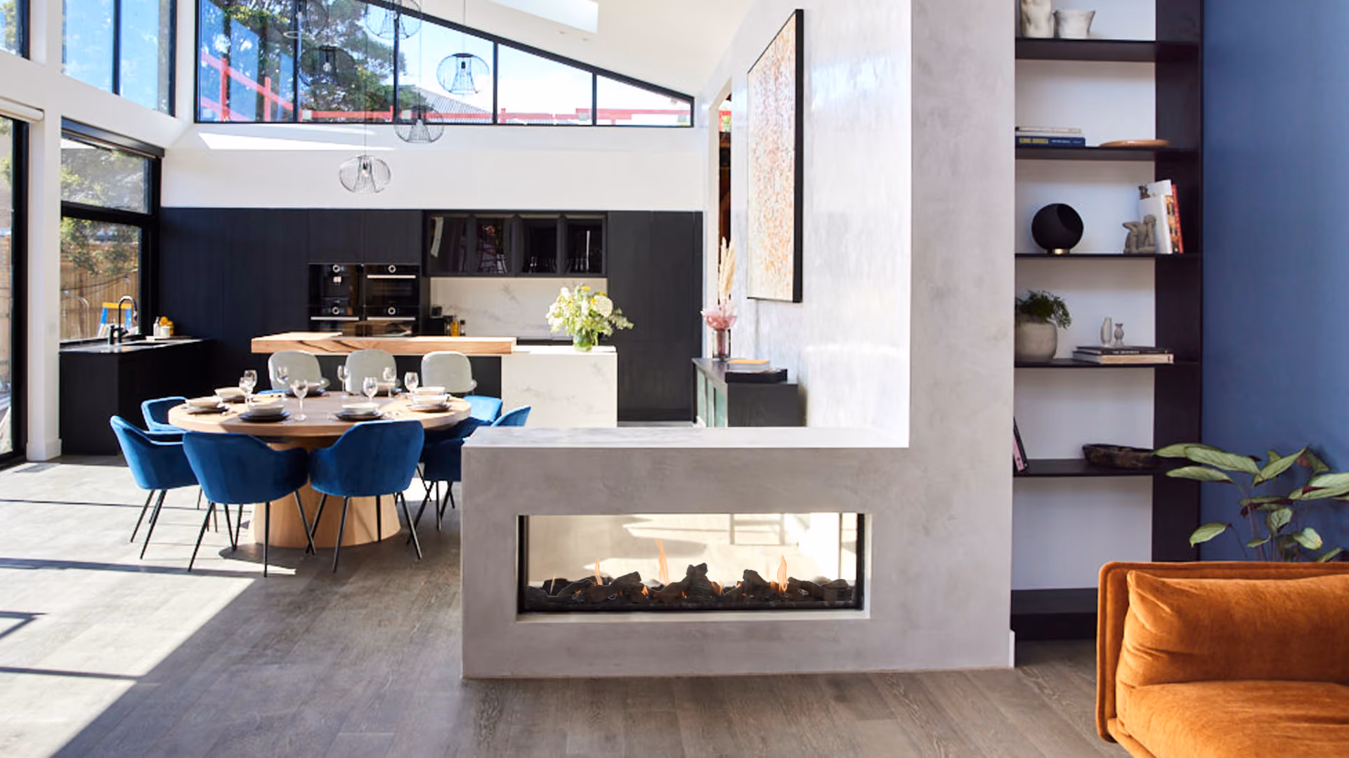 Modern gas fireplace with realistic burning logs set in a light-coloured wall next to a wooden side table with books.