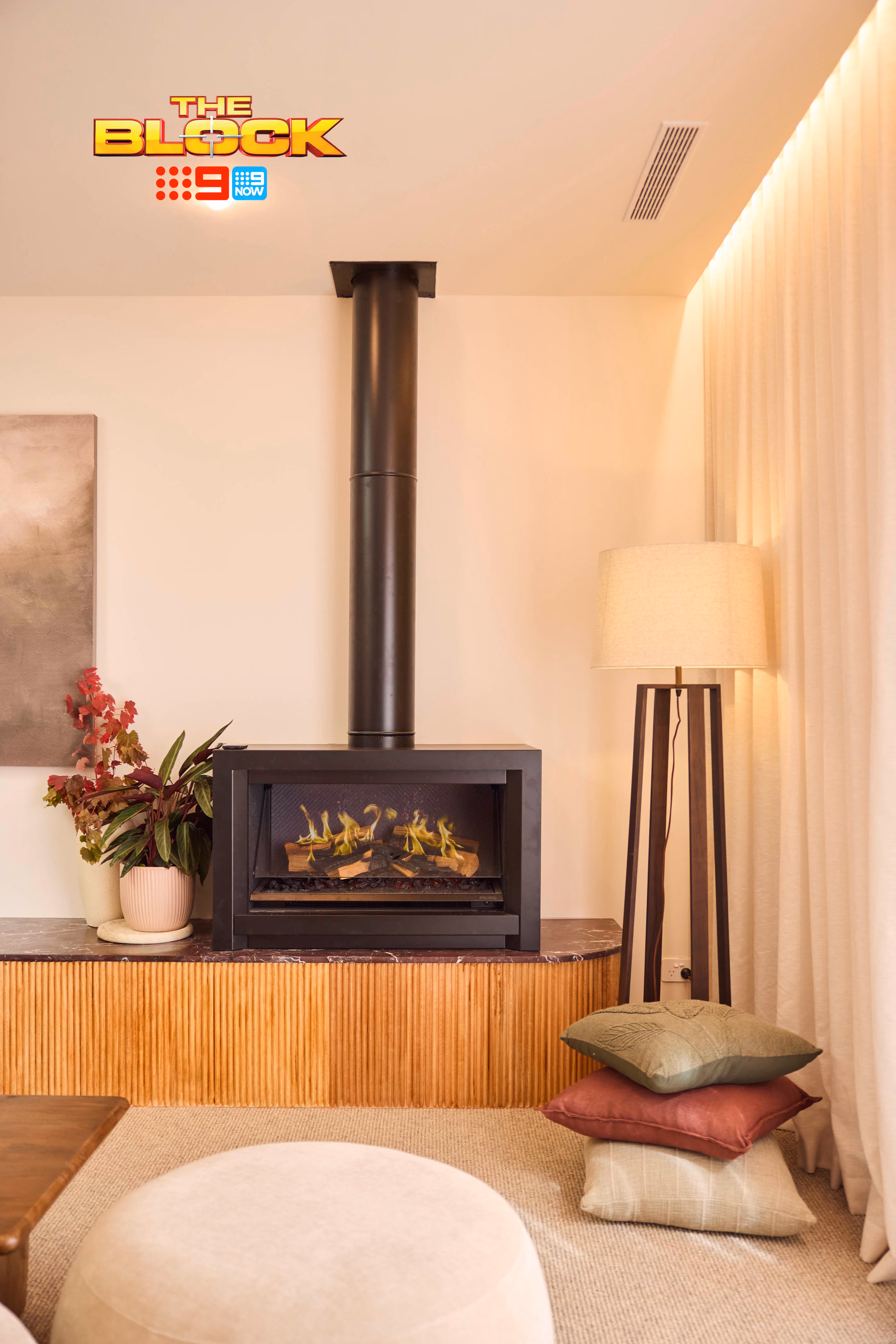 Modern gas fireplace with realistic burning logs set in a light-coloured wall next to a wooden side table with books.