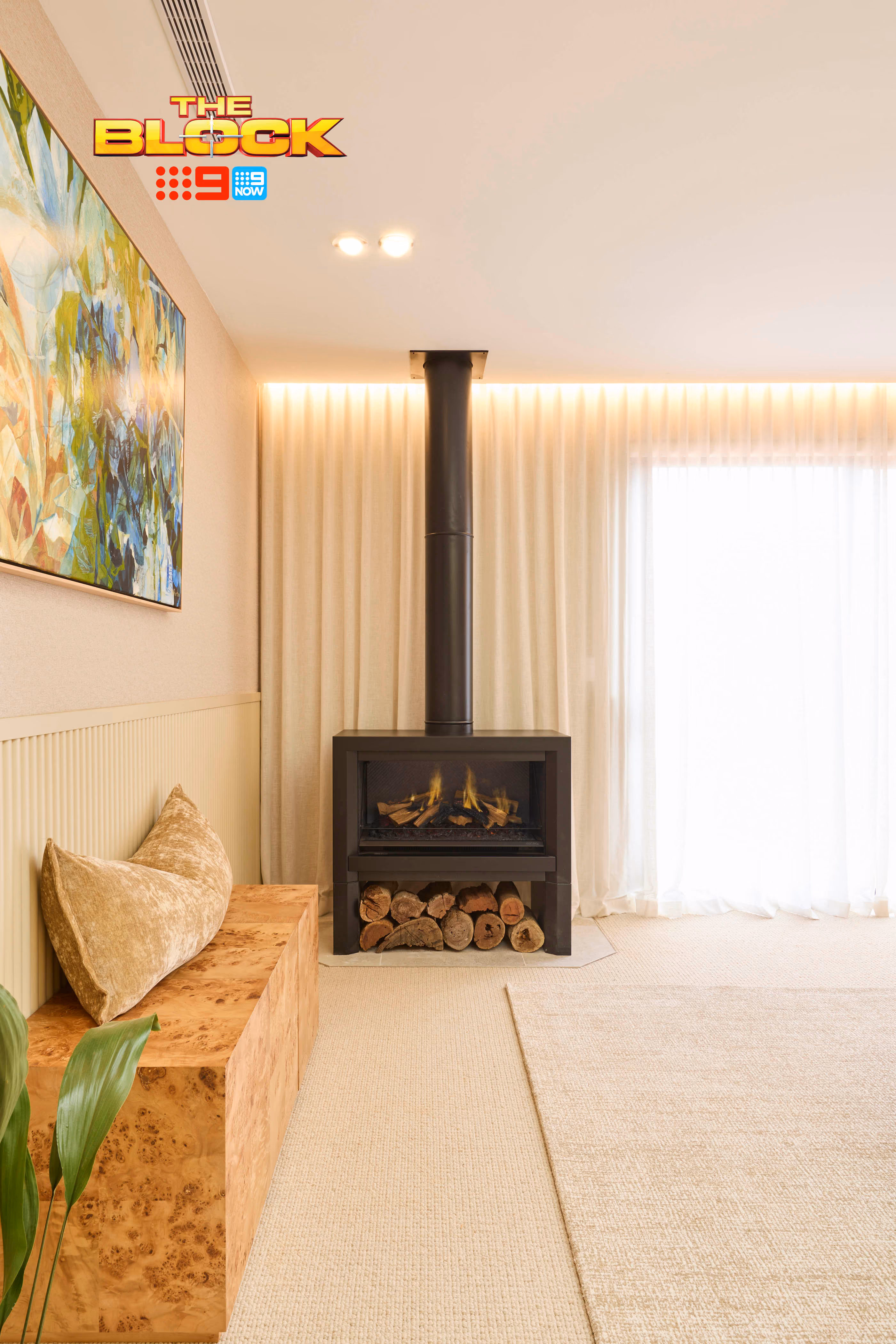Modern gas fireplace with realistic burning logs set in a light-coloured wall next to a wooden side table with books.
