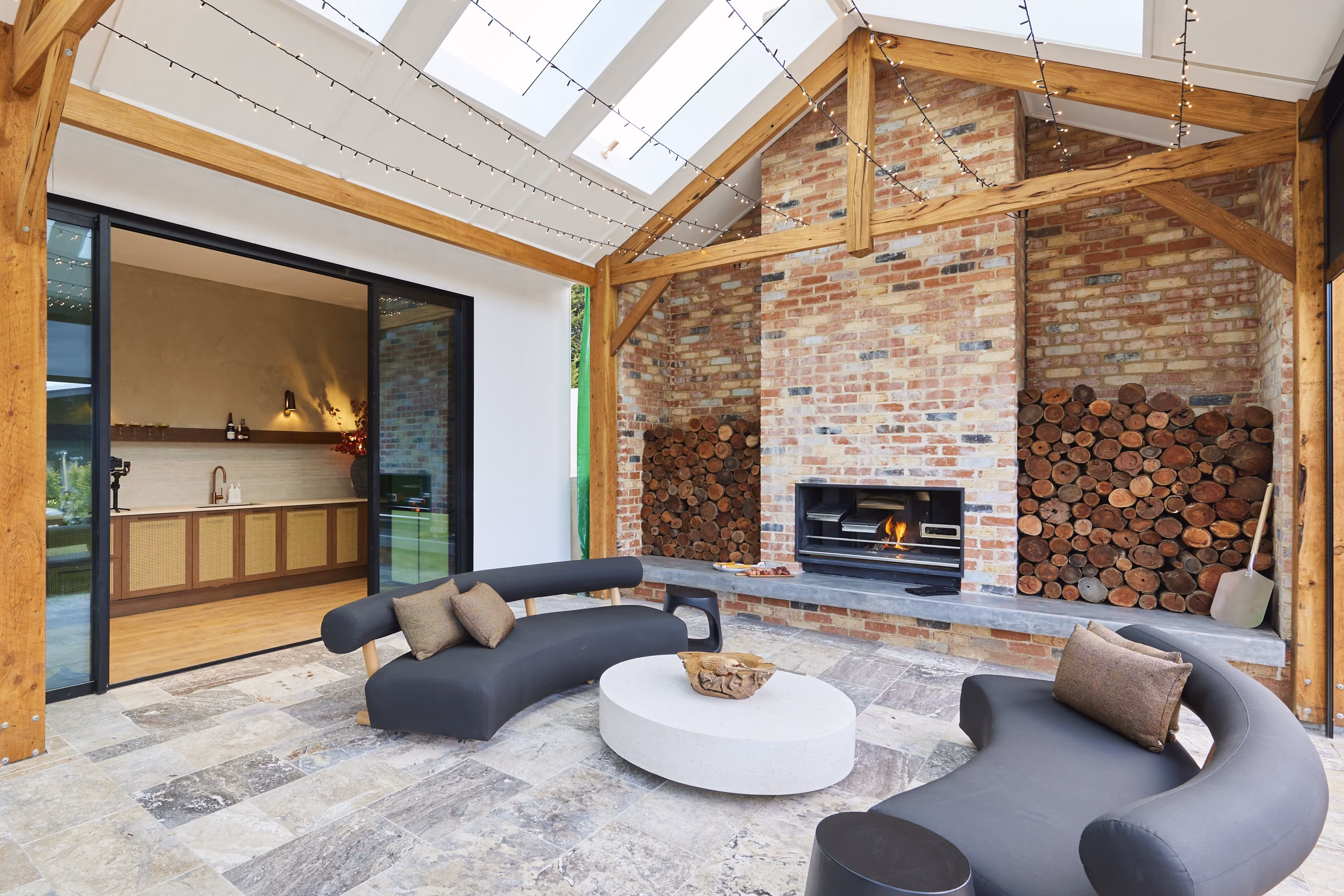 Modern gas fireplace with realistic burning logs set in a light-coloured wall next to a wooden side table with books.