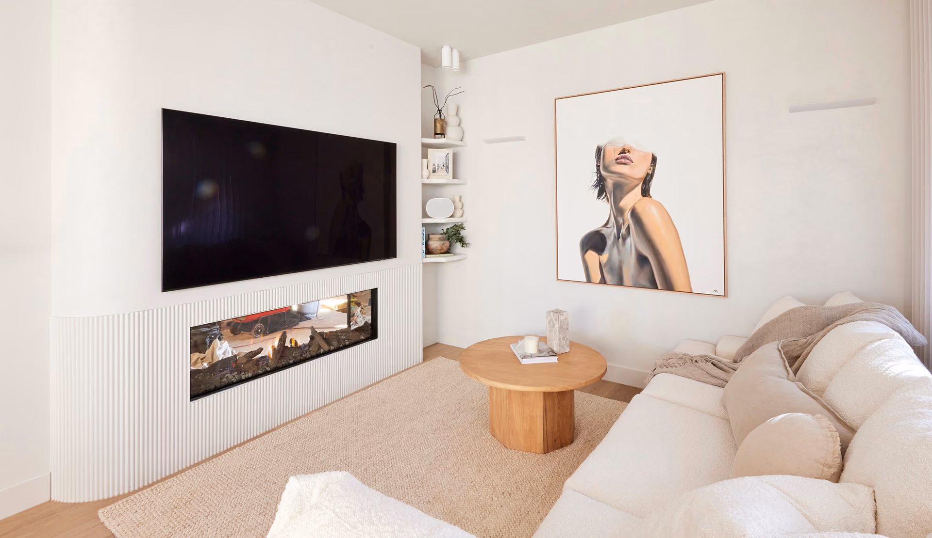 Modern gas fireplace with realistic burning logs set in a light-coloured wall next to a wooden side table with books.