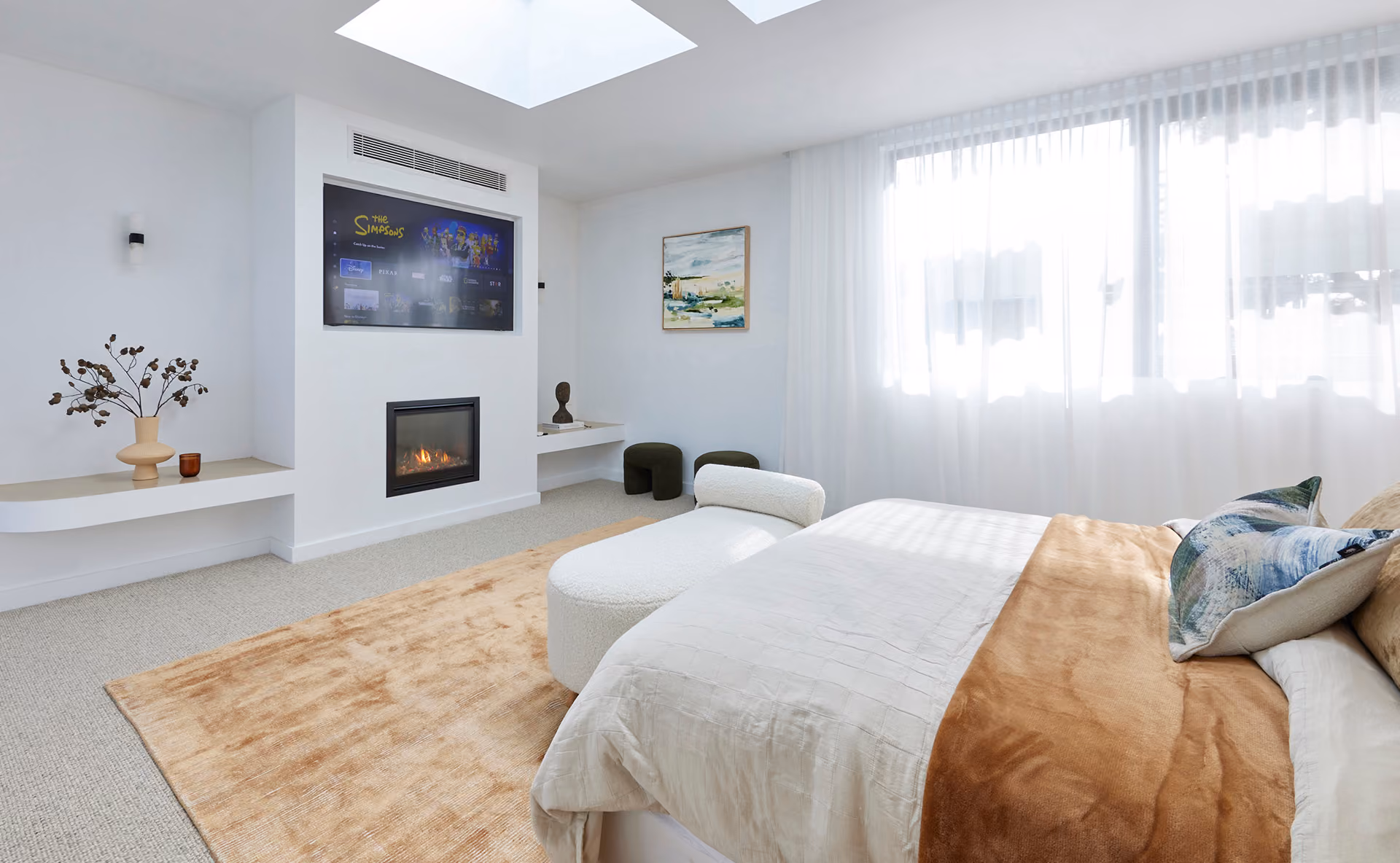 Modern gas fireplace with realistic burning logs set in a light-coloured wall next to a wooden side table with books.