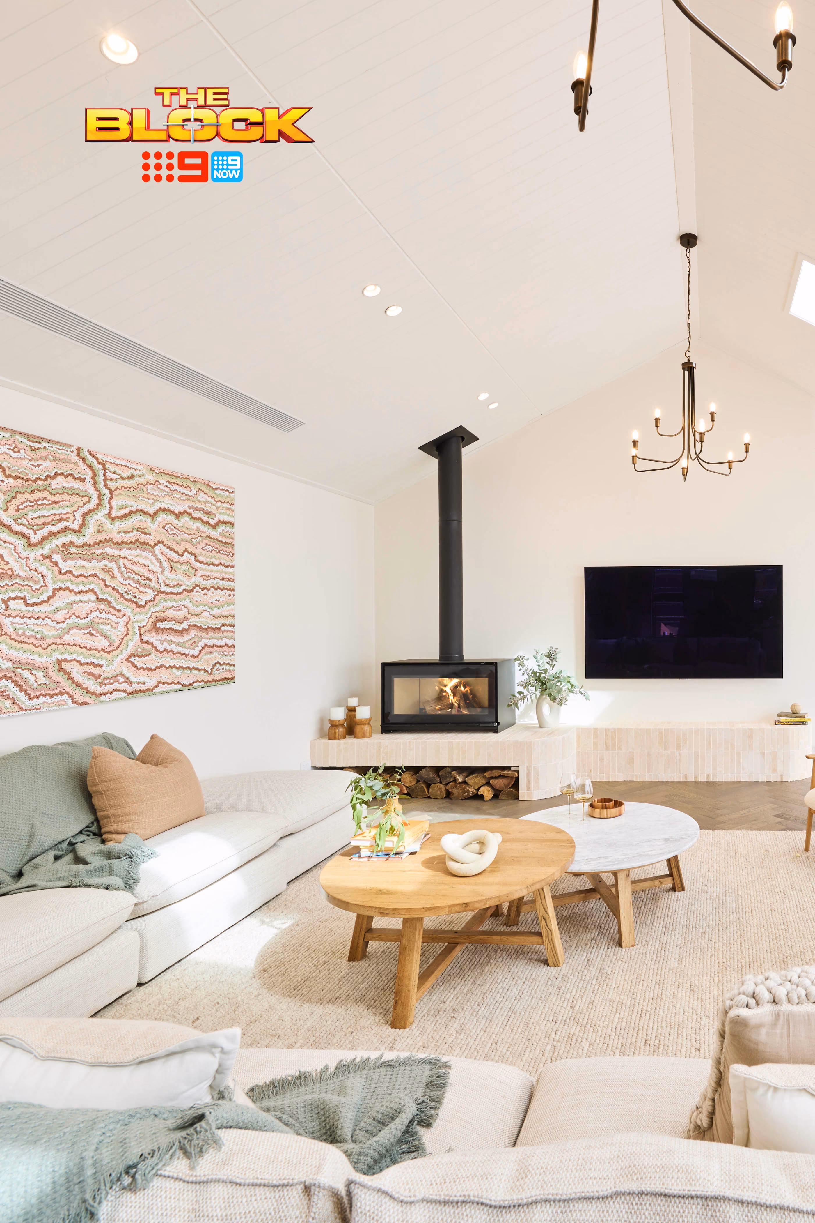 Modern gas fireplace with realistic burning logs set in a light-coloured wall next to a wooden side table with books.